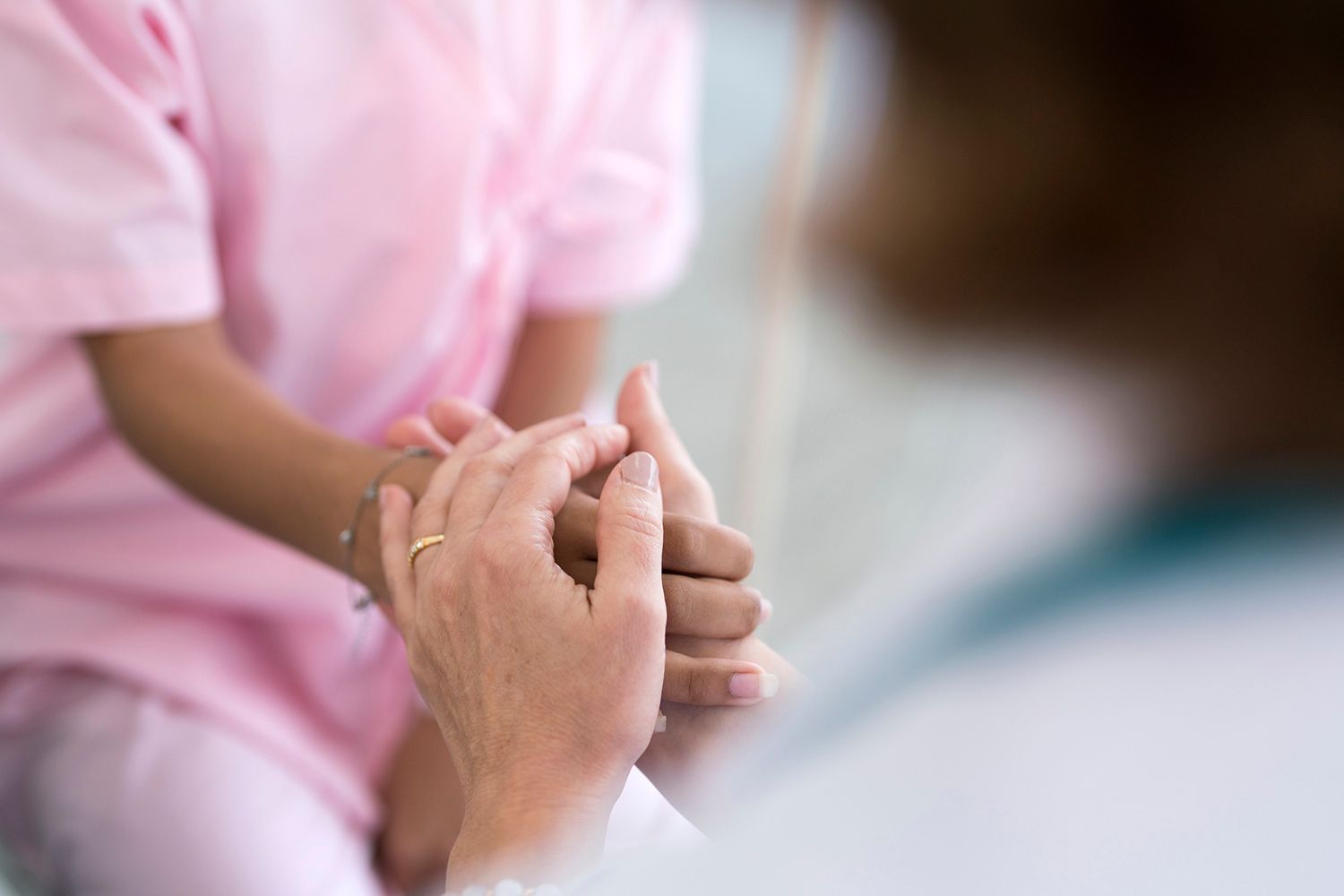 Person in pink scrubs, hands held by another, offering comfort.