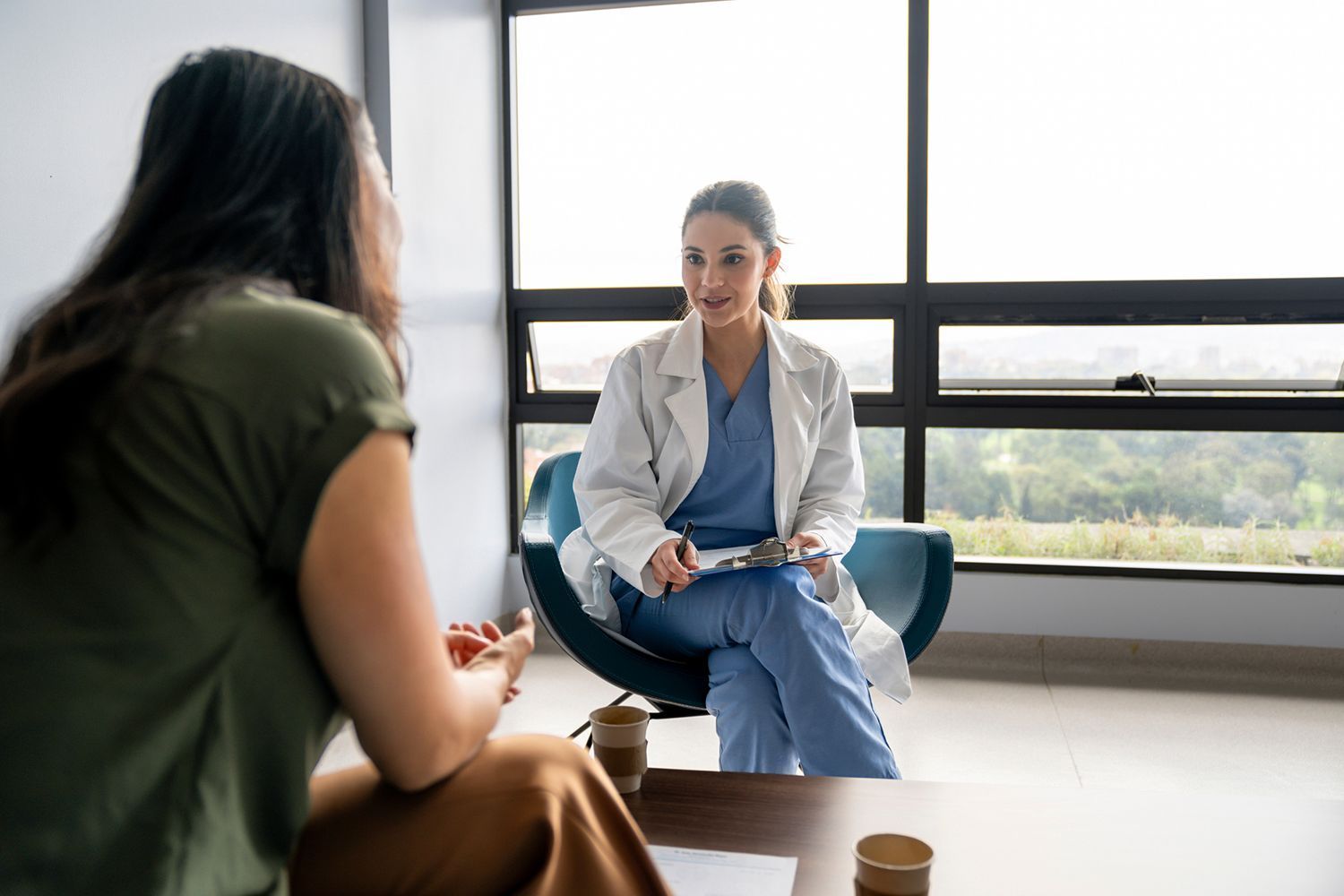 A woman consults with a healthcare professional in a clinic. The professional holds a clipboard.