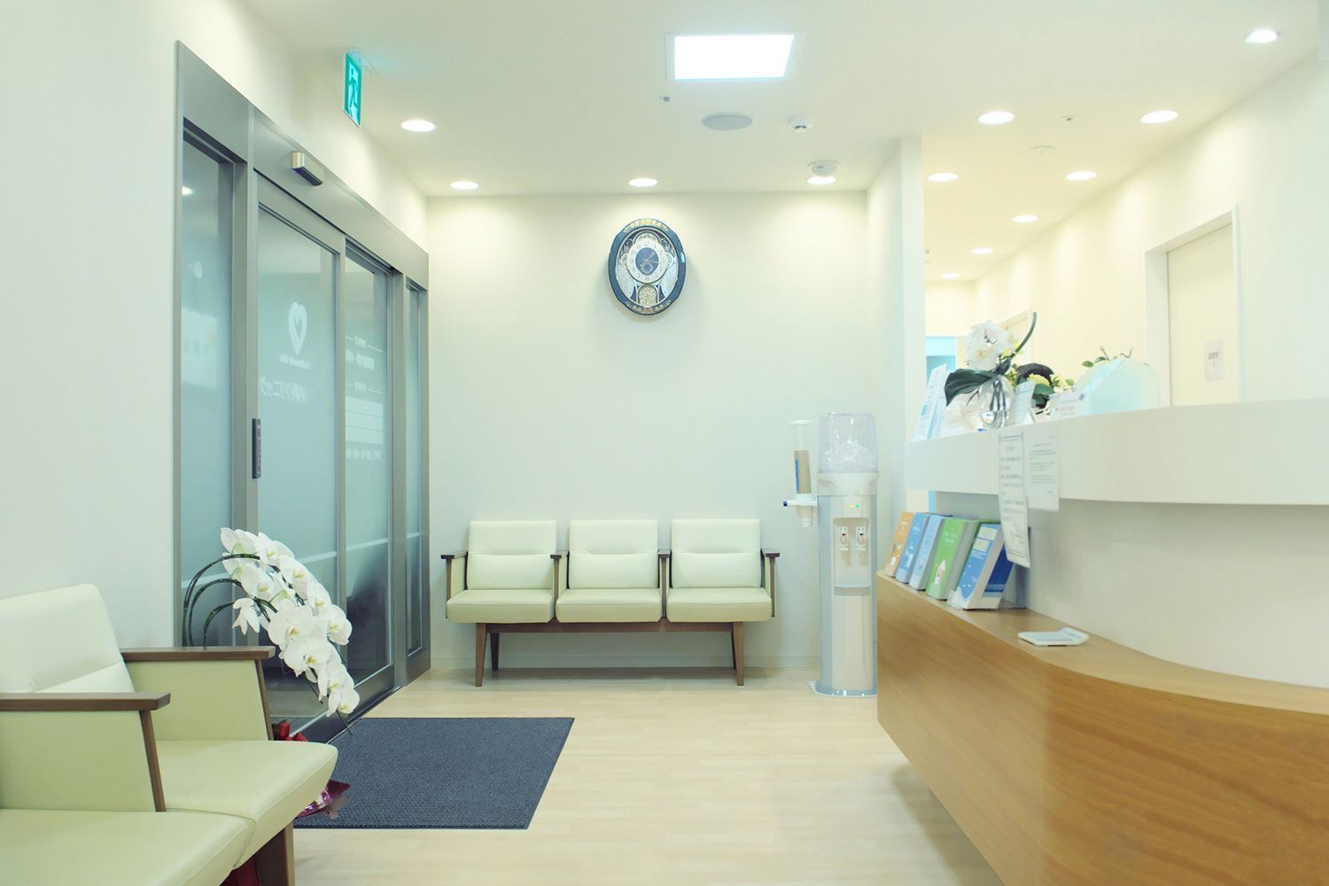 Brightly lit doctor's office waiting room with chairs, reception desk, and glass doors.