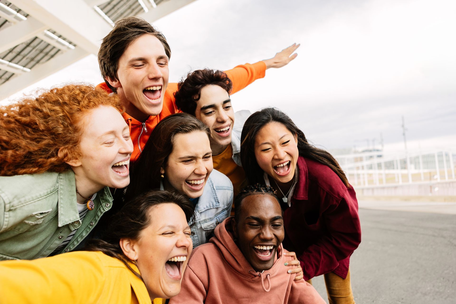 Group of diverse young people laughing, posing close together outdoors.