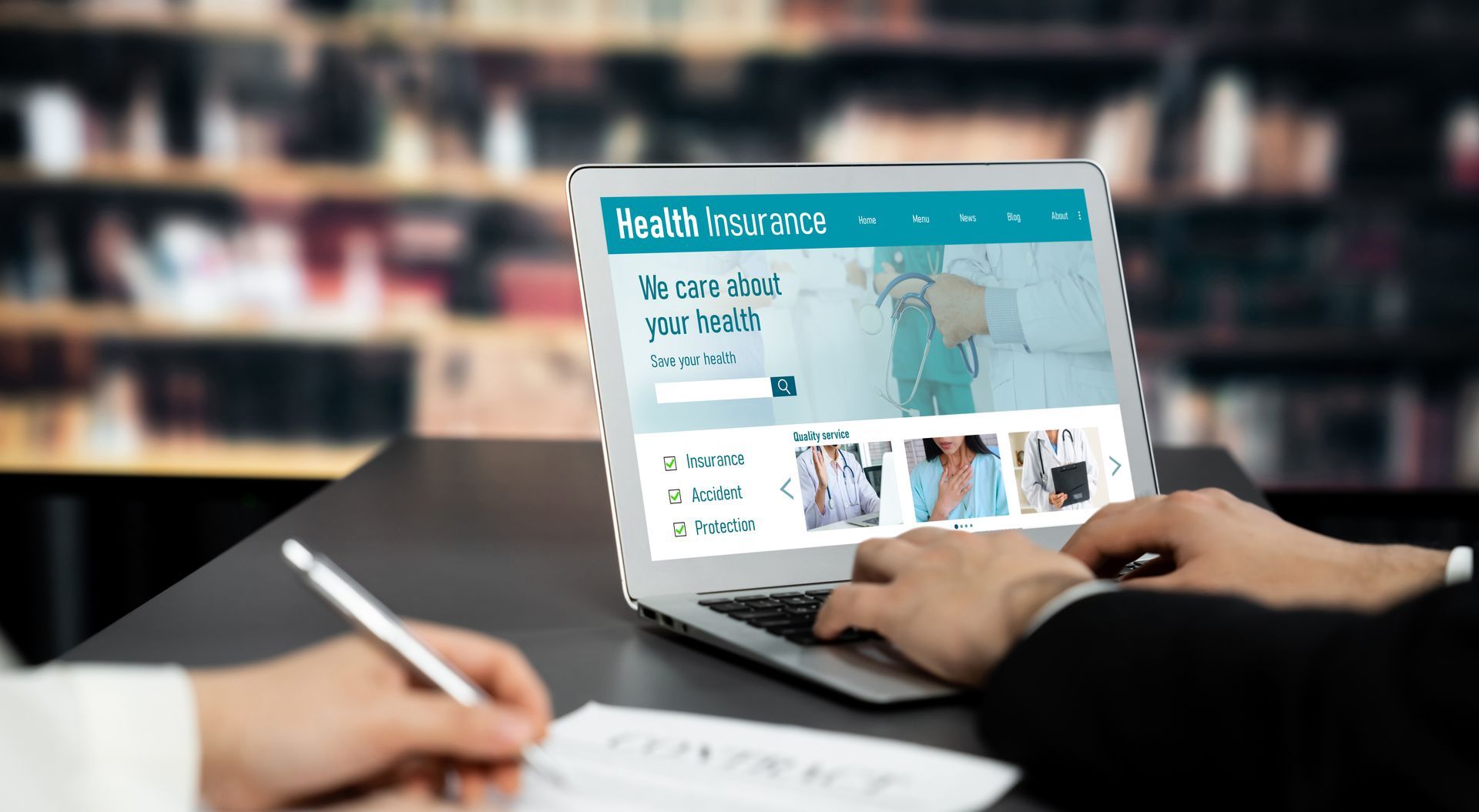 Hands using a laptop showing a website. Someone takes notes at a desk in a library. Hands using a laptop showing a website. Someone takes notes at a desk in a library.