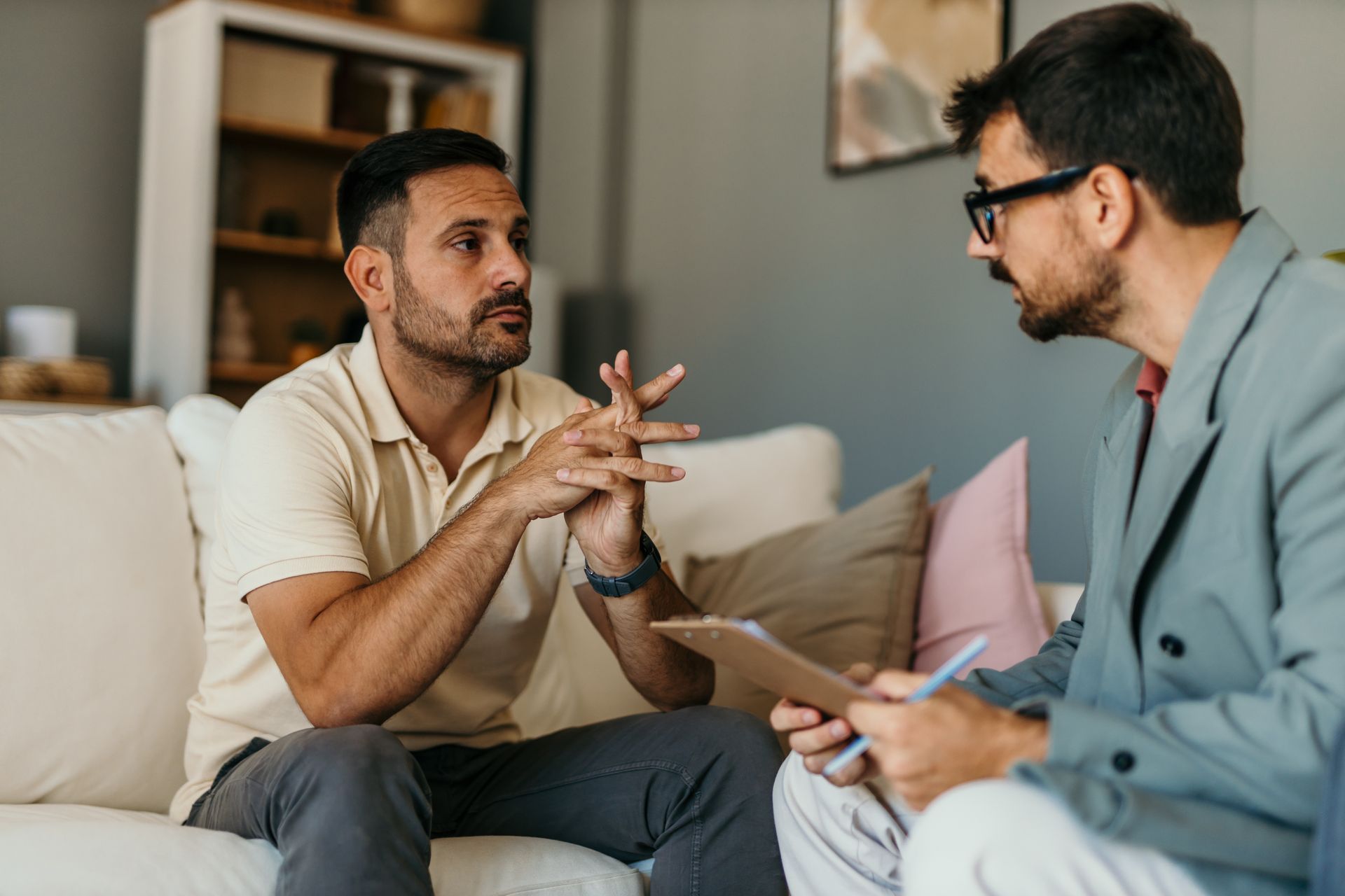 Man on a couch talking to a person holding a clipboard; indoor setting. Man on a couch talking to a person holding a clipboard; indoor setting.