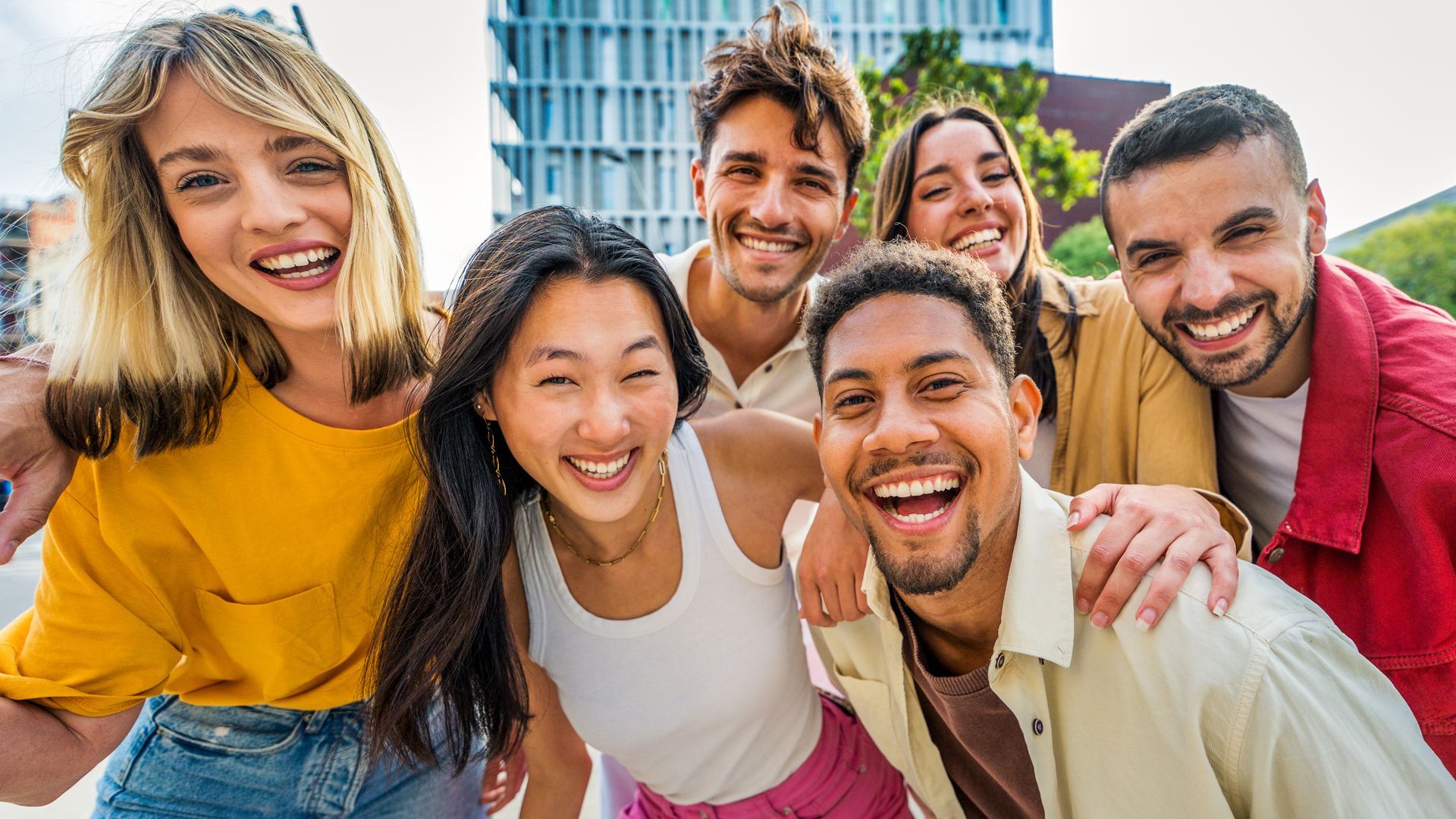Group of smiling people pose for a photo outdoors, near a building.