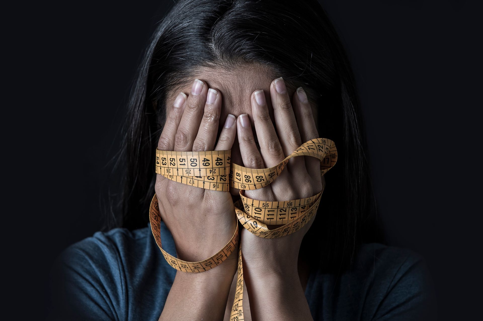 Woman covering face with hands wrapped in measuring tape.