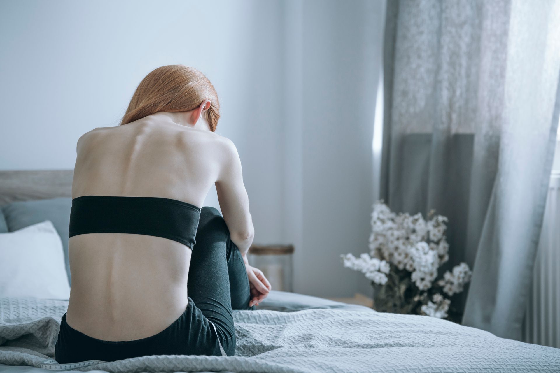 Person with visible ribs sits on bed, facing away.