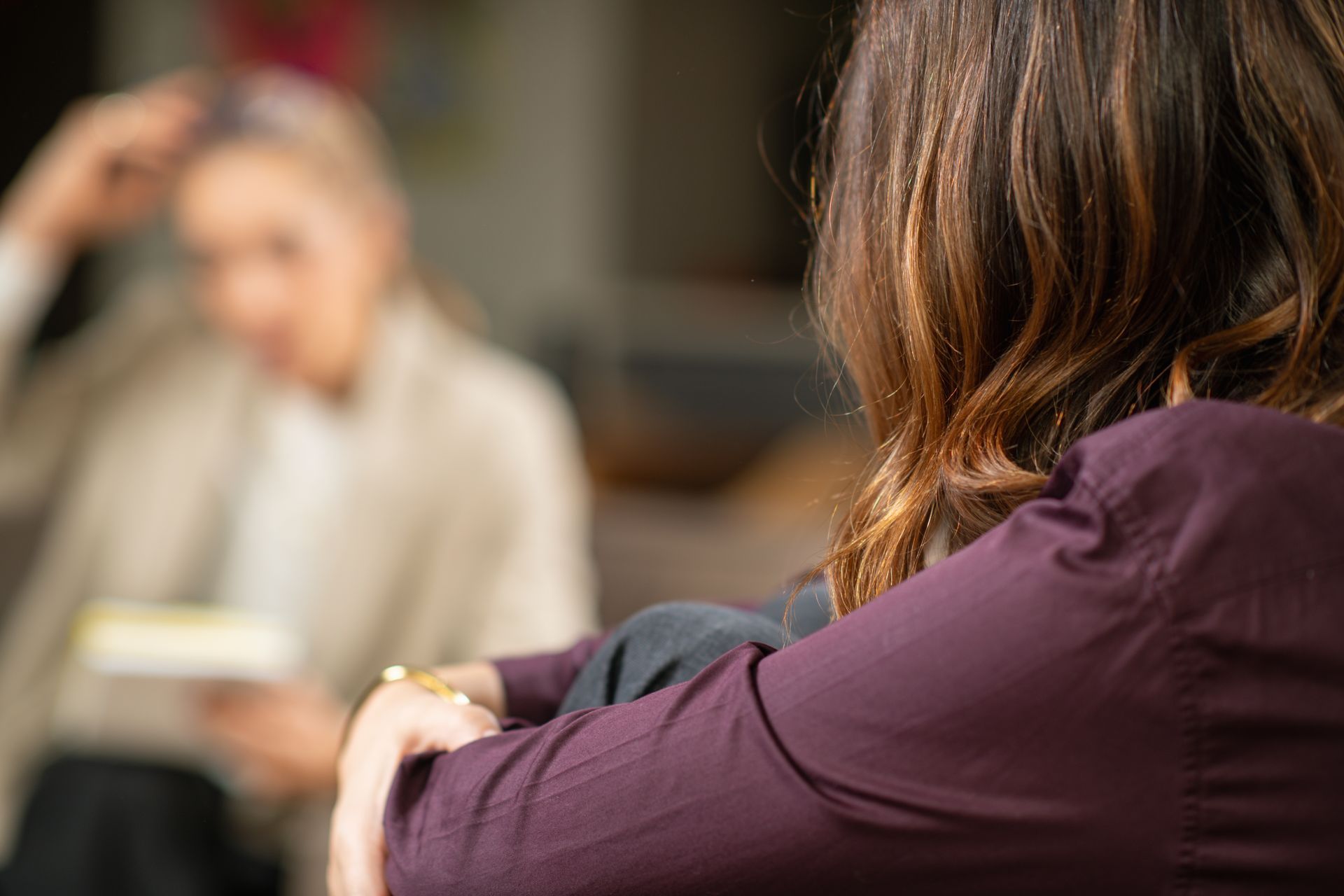 Woman in purple shirt in therapy session, facing therapist who holds notes. Woman in purple shirt in therapy session, facing therapist who holds notes.