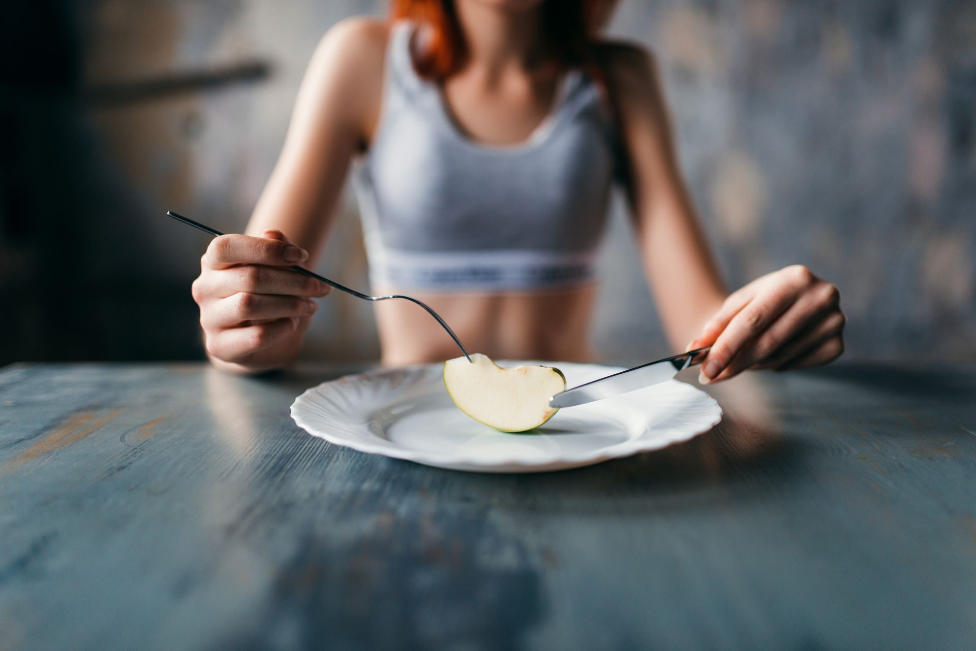 Woman seated at a table with an apple slice on a plate, using a fork and knife.