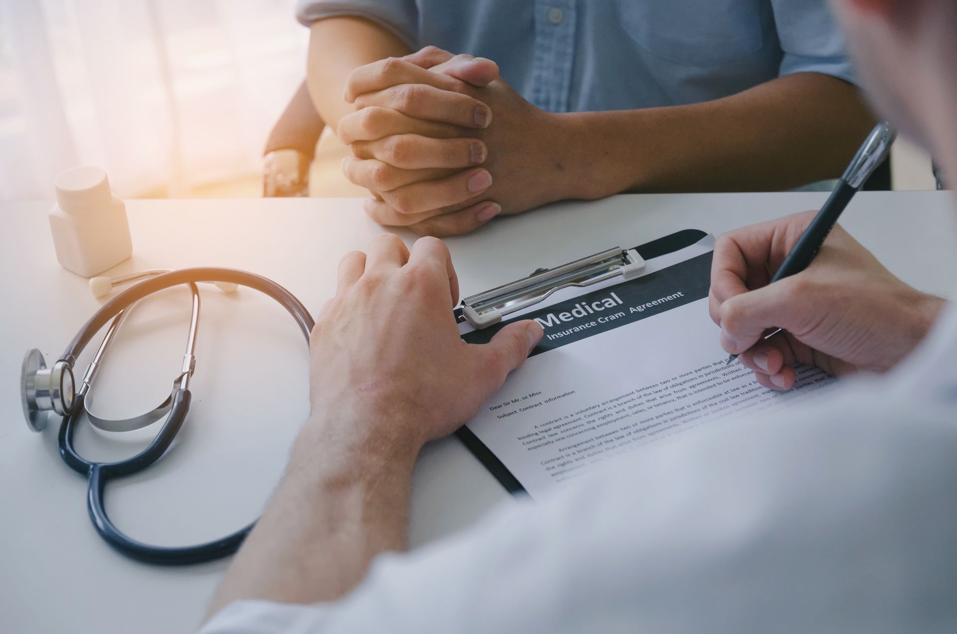 Doctor writing on medical form with a stethoscope on a desk, interviewing a patient.