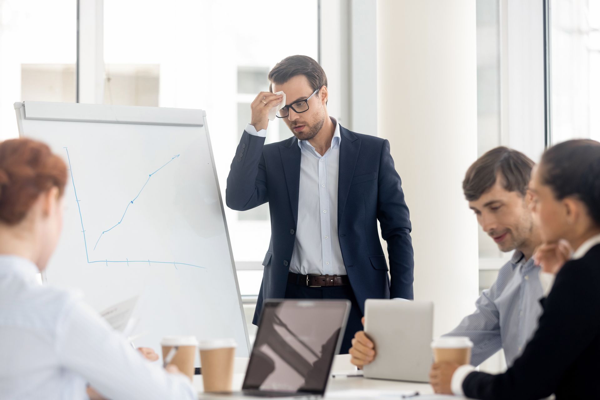 Man sweating while presenting a graph to colleagues in a bright office.