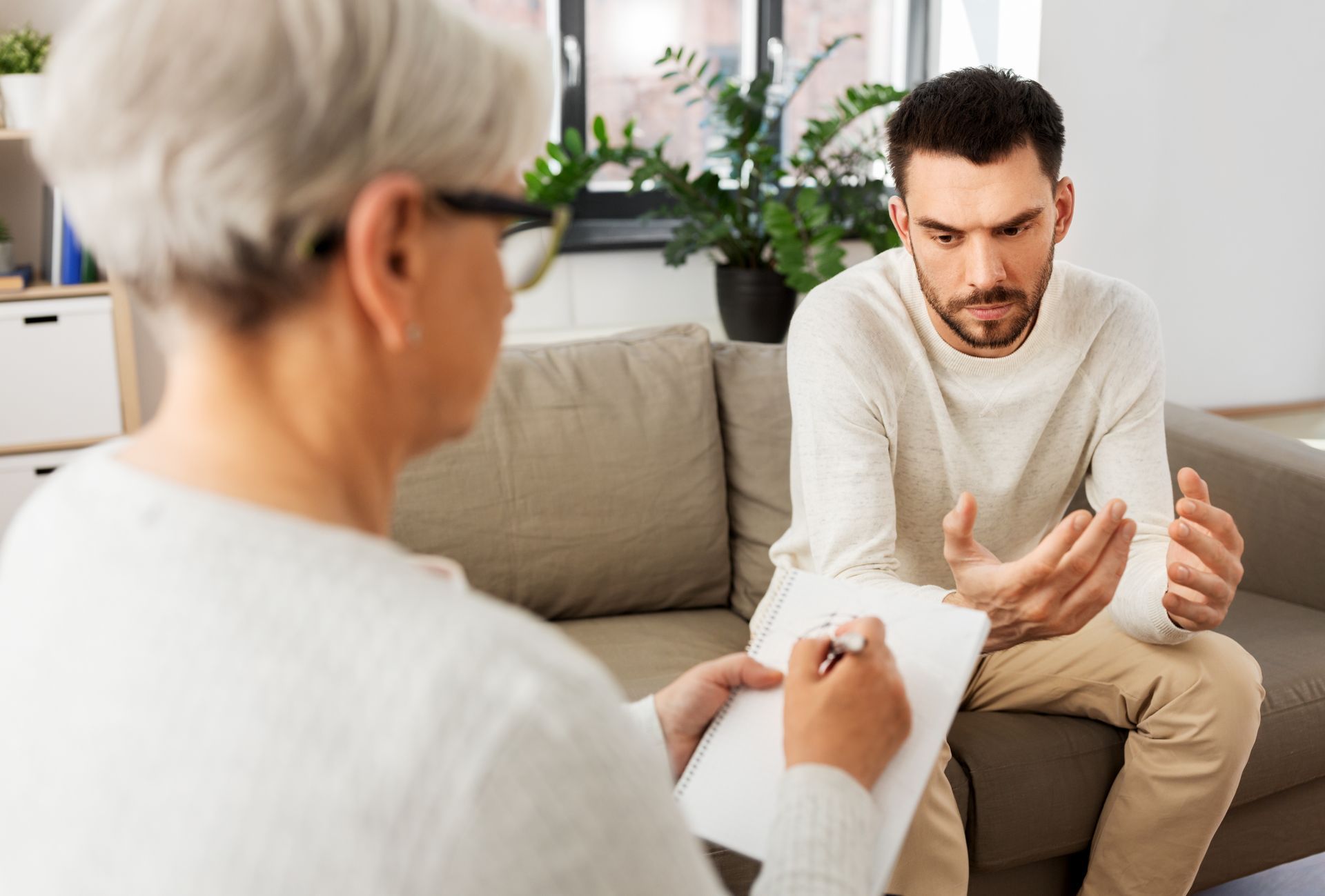 Therapist taking notes during a counseling session with a client; both seated on a couch. Therapist taking notes during a counseling session with a client; both seated on a couch.