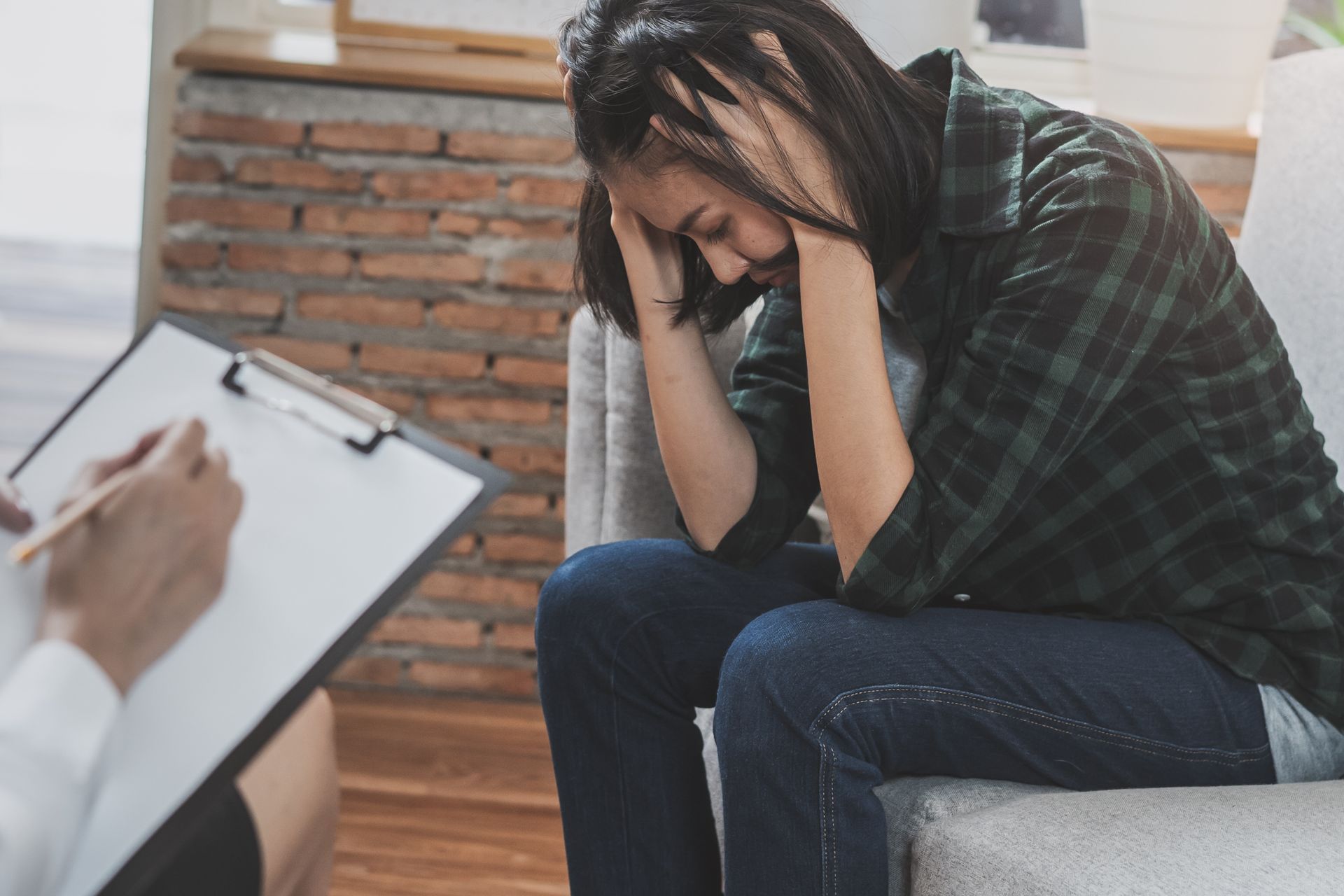 Woman in distress, hands on head, sits while someone takes notes on a clipboard in a therapist's office. Woman in distress, hands on head, sits while someone takes notes on a clipboard in a therapist's office.