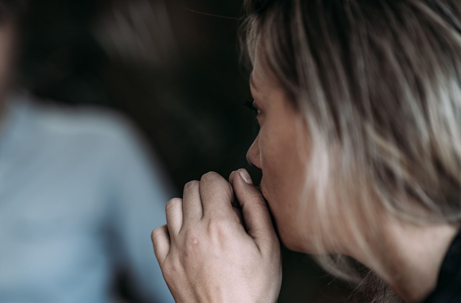 Woman in distress, covering her mouth, talking to therapist in a blurred office setting.