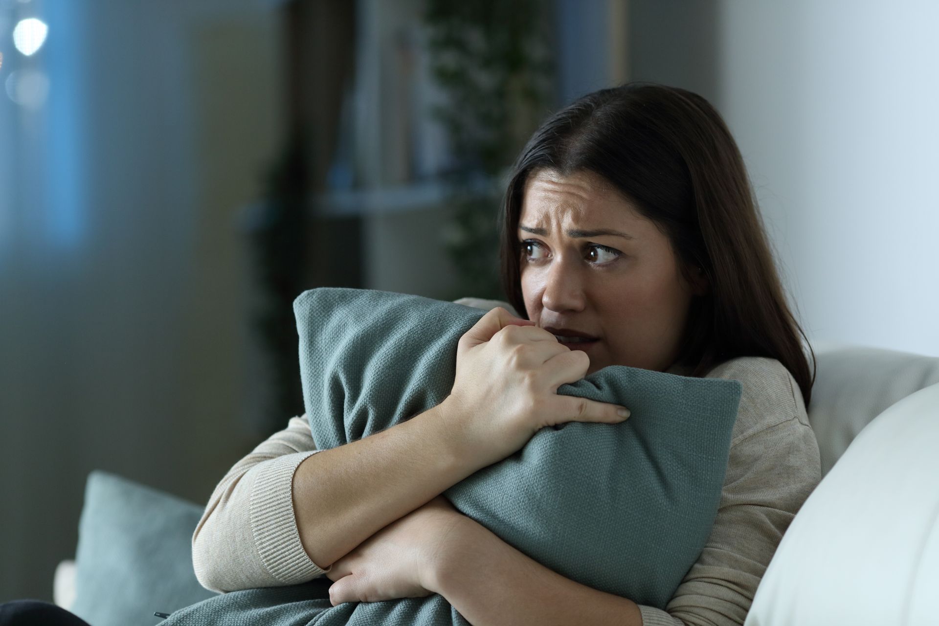 Woman with anxious expression, clutching a pillow in a dimly lit room.