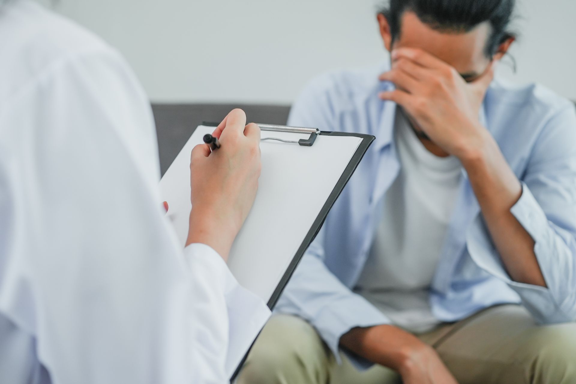 Person in distress seated during a session with a medical professional taking notes.