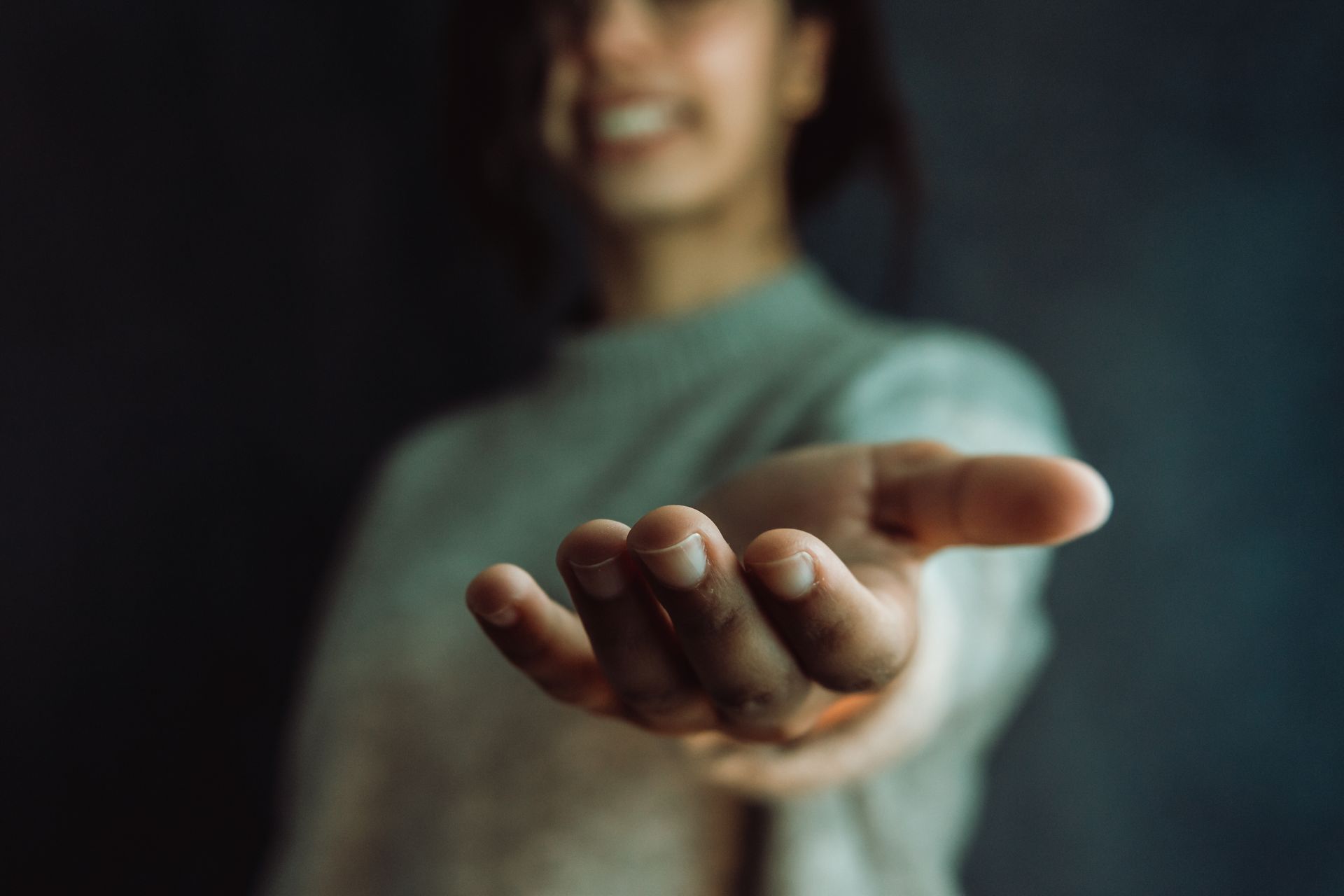 Person extending hand, smiling, blurred background. Person extending hand, smiling, blurred background.