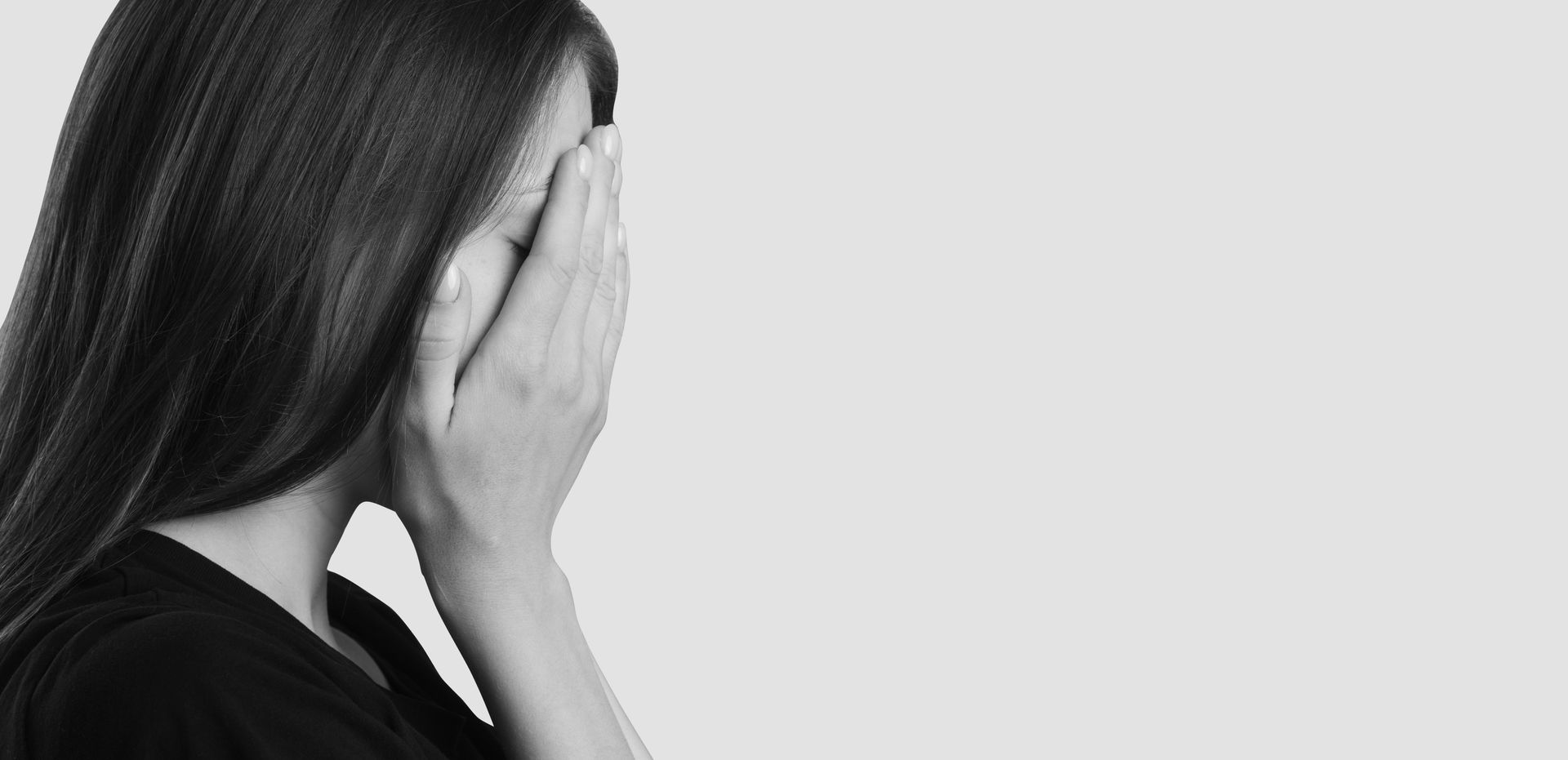 Woman covering face with hands, in profile. Black and white, plain background.