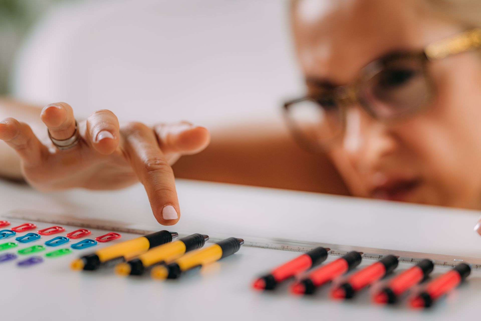 Woman reaching toward yellow markers on a table, with a confused expression.