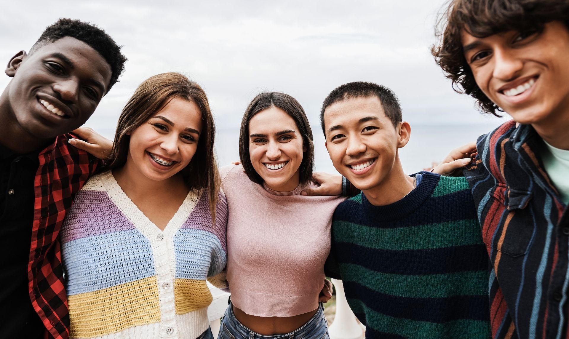 Group of smiling friends with arms around each other, outdoors with a neutral background.
