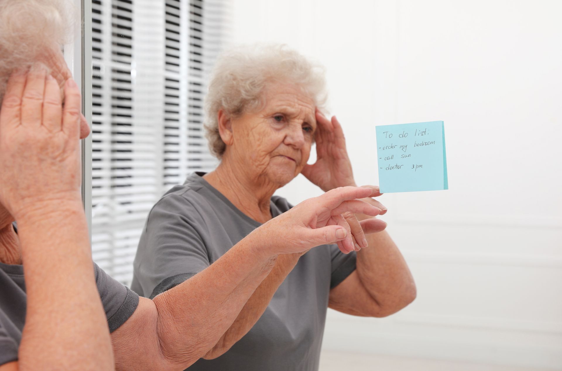Woman looking in mirror with a post-it note, appearing confused.
