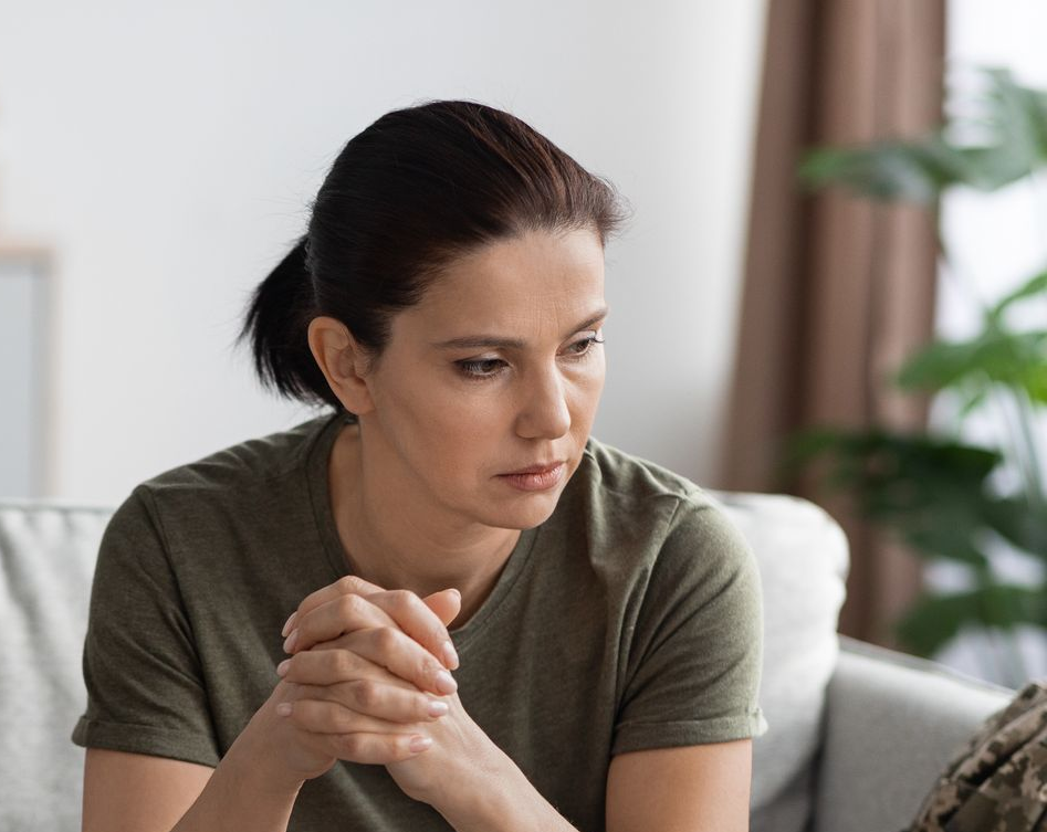 Woman in military fatigues on a sofa, looking pensive during a therapy session.