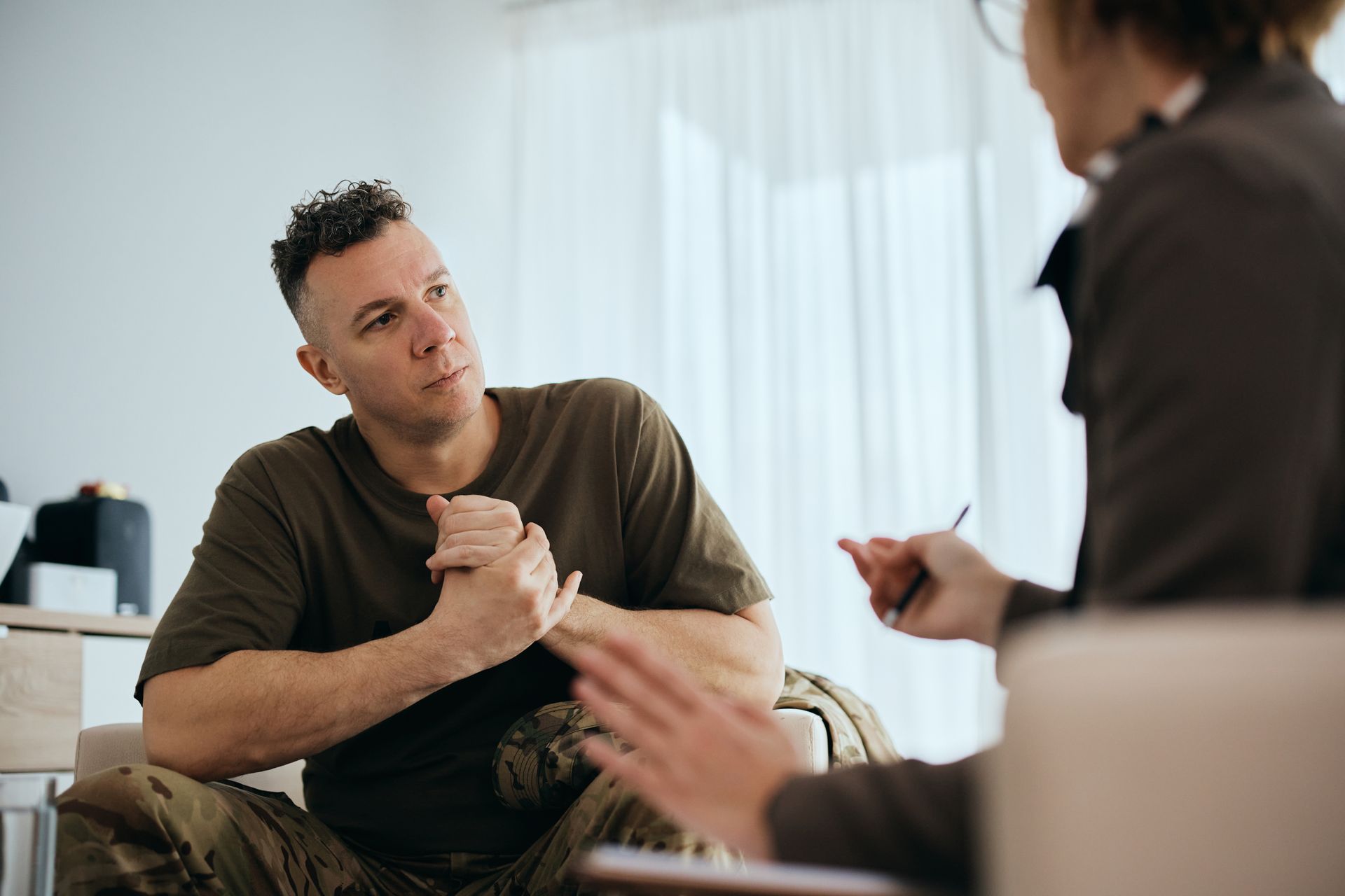 Man in military fatigues talking to a therapist in a brightly lit room.