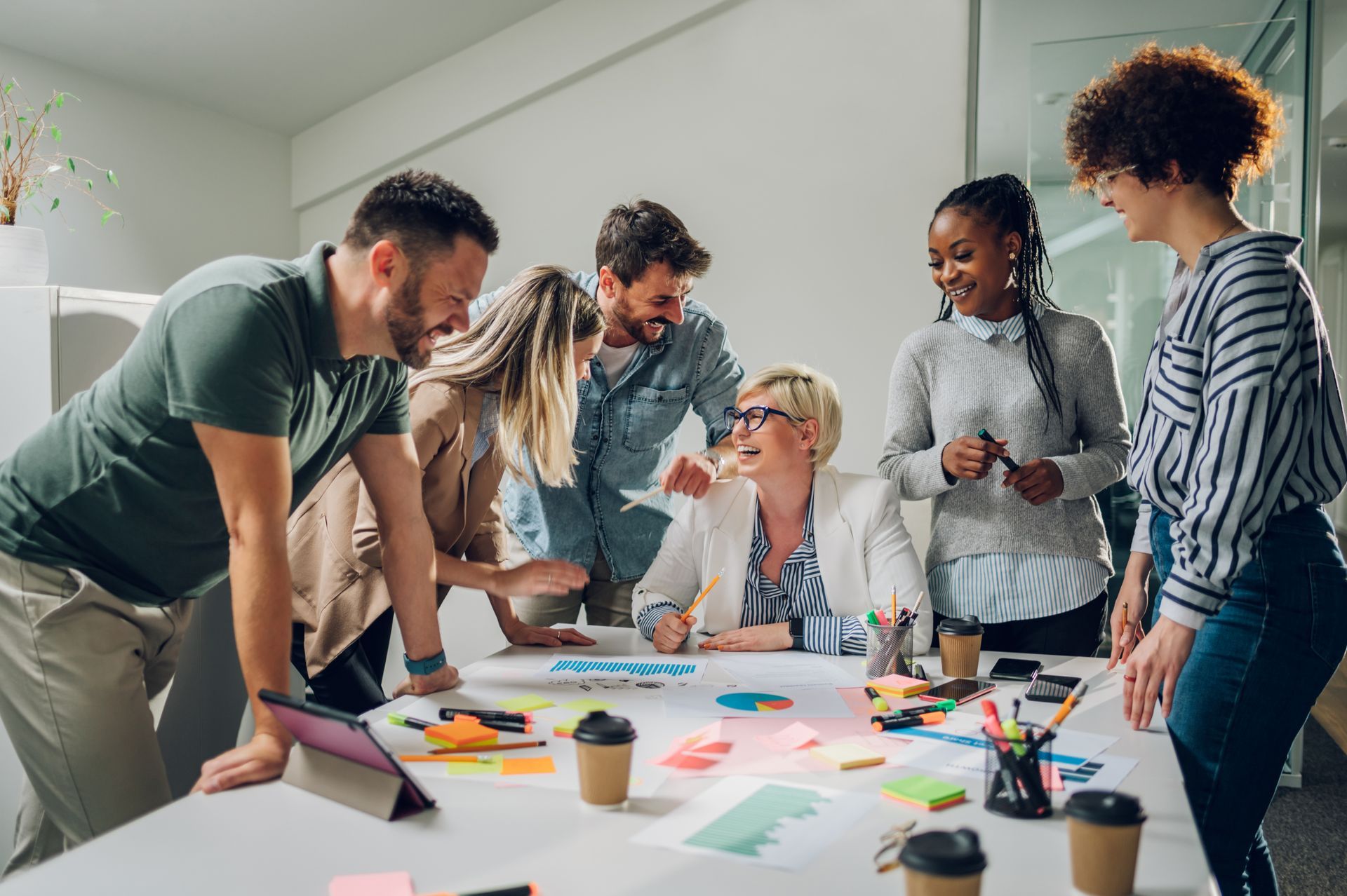 A team collaborates around a table with colorful sticky notes and coffee cups in an office.