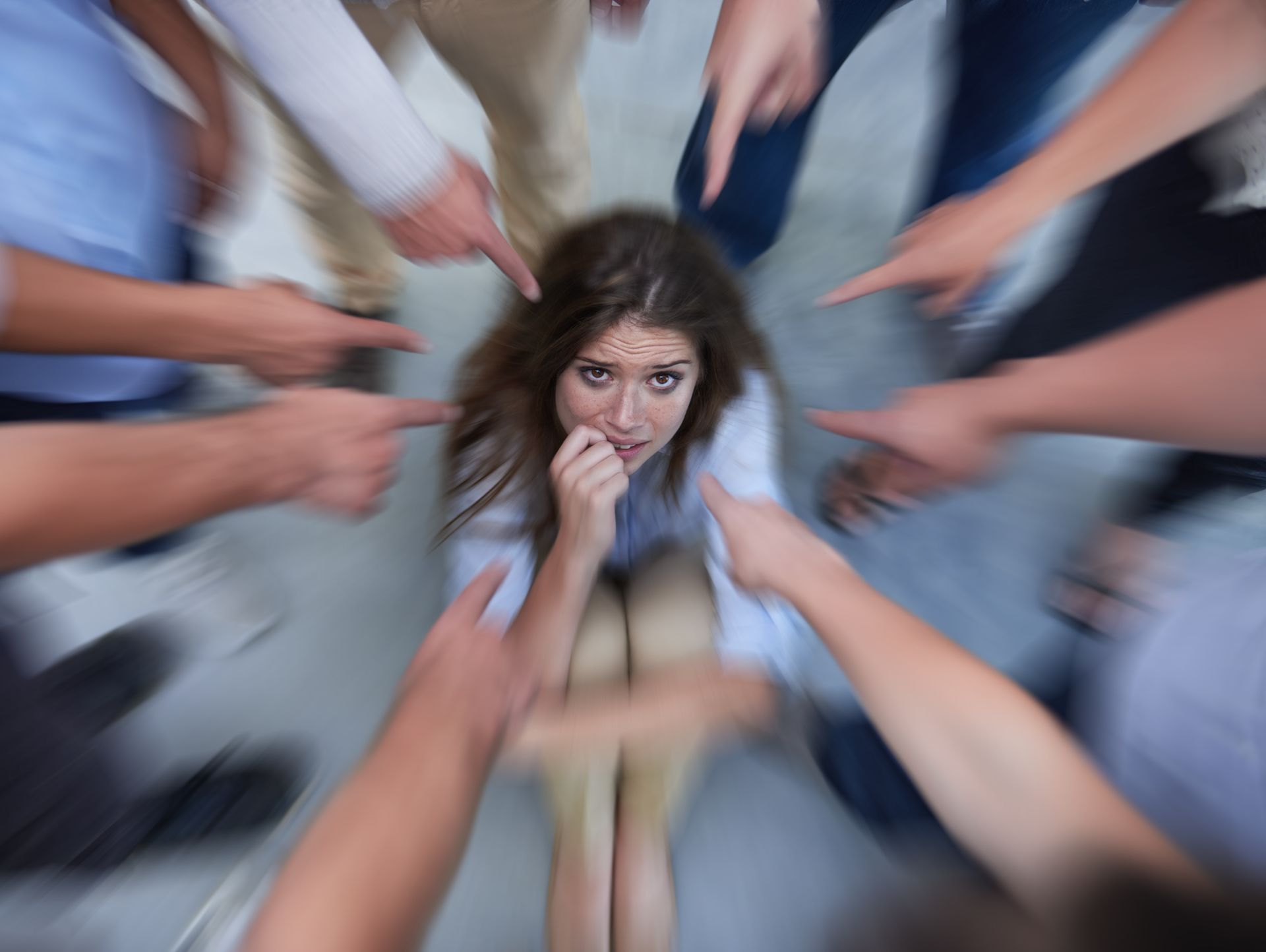 Woman looks frightened, surrounded by blurred hands pointing towards her.