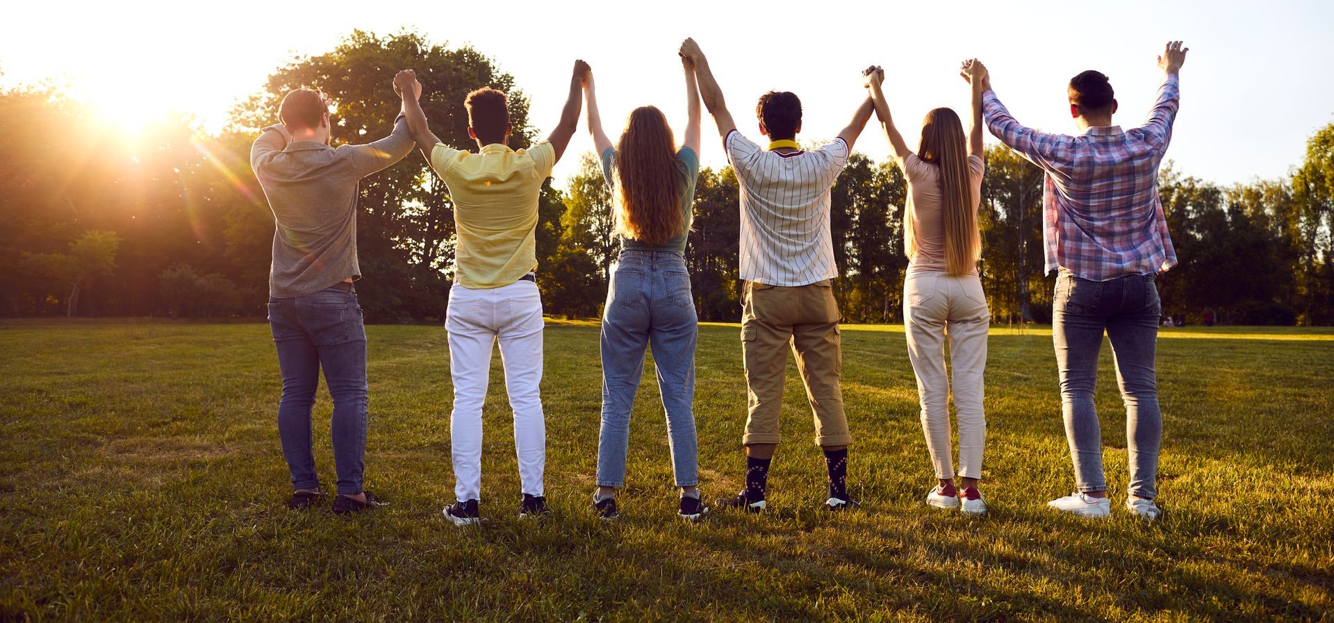 Seven people holding hands, standing in a field with their arms raised. Sun in background. Seven people holding hands, standing in a field with their arms raised. Sun in background.