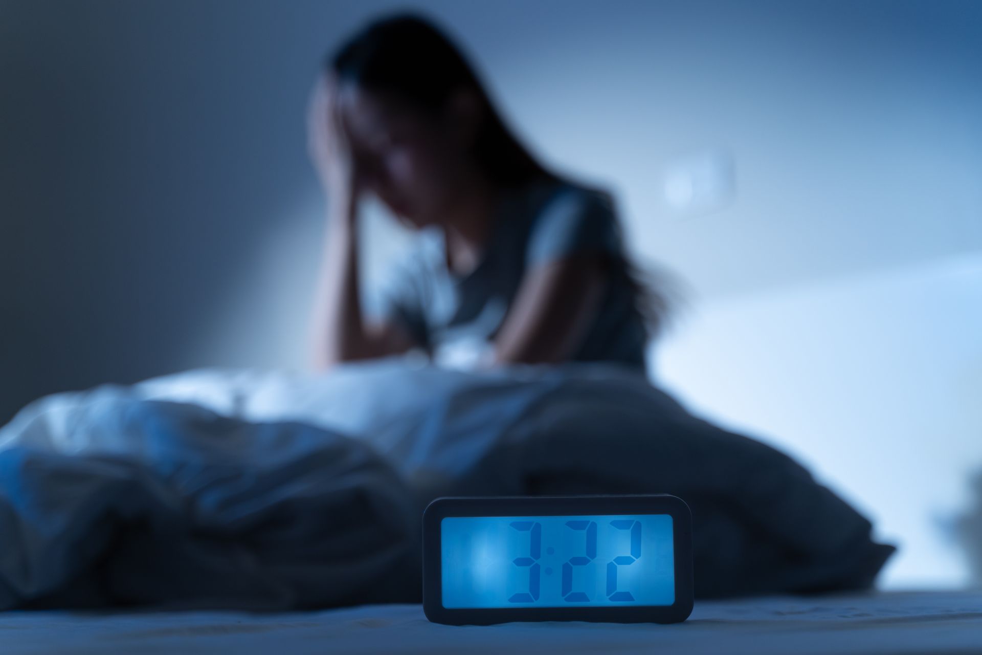 Woman in bed with digital clock showing 3:22 AM, looking stressed. Dark blue and white setting.