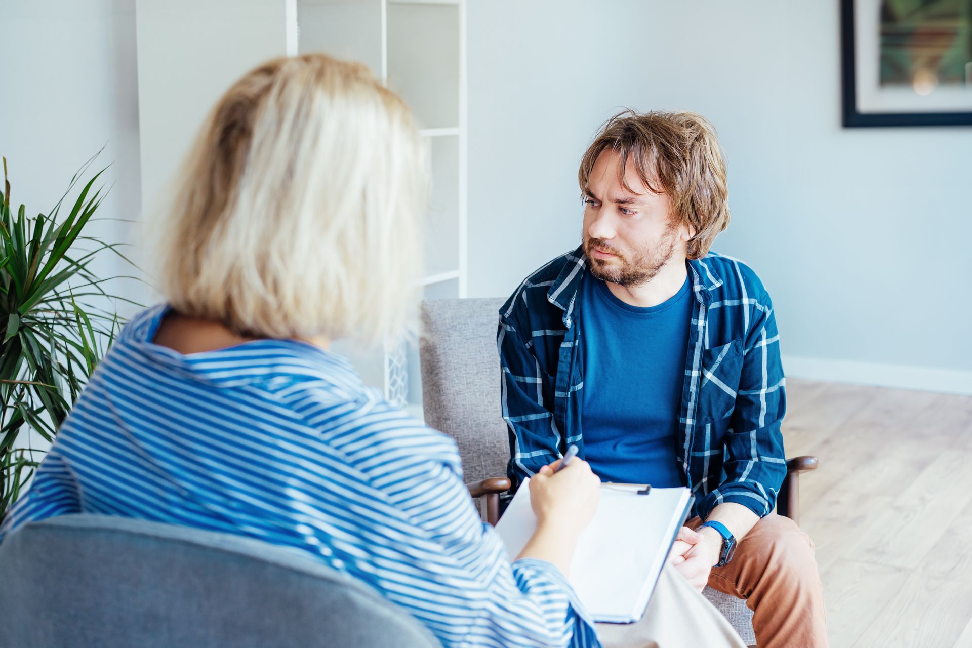 Therapist and patient in a counseling session; patient looks concerned, therapist takes notes.