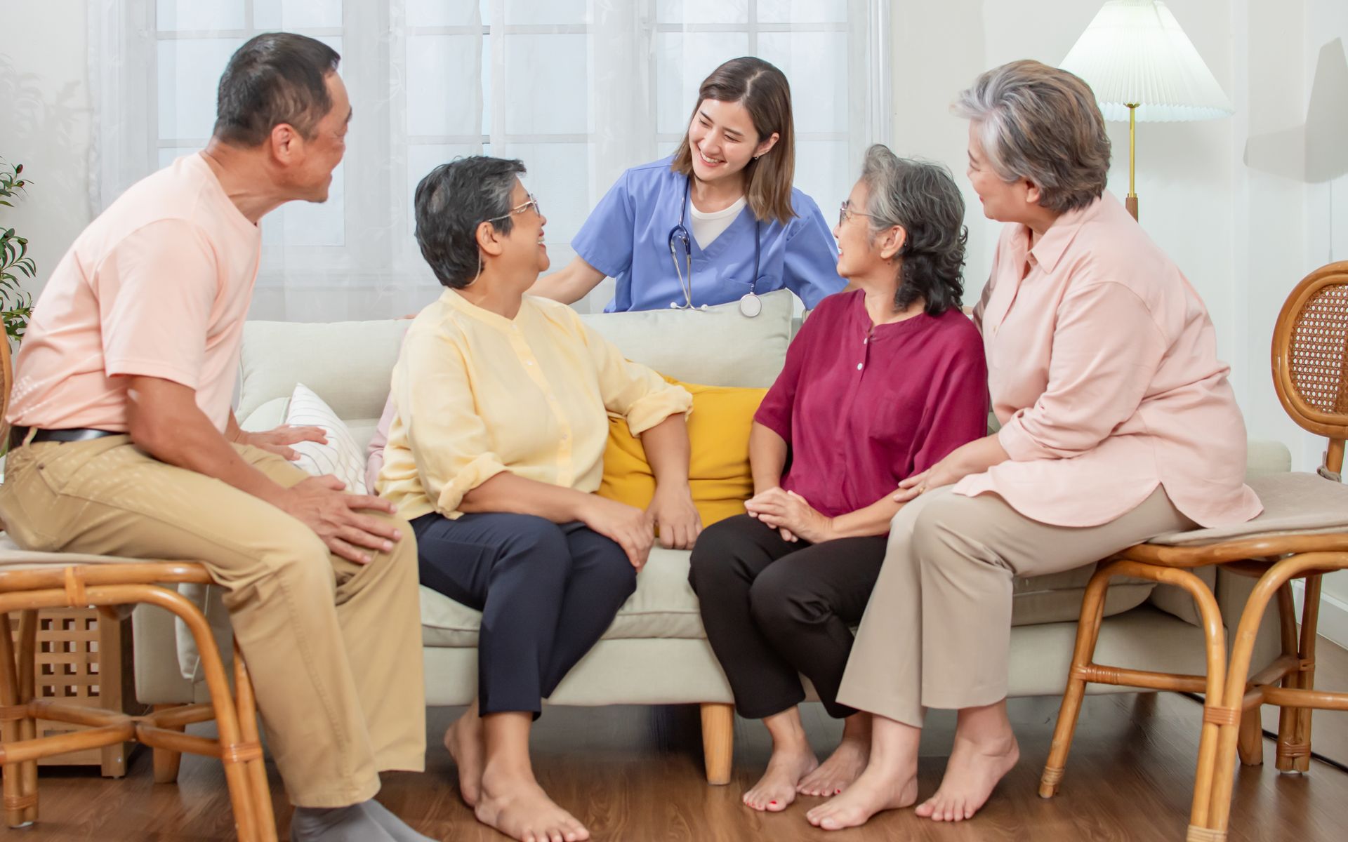 A group of people sitting with a healthcare worker in a living room, smiling and talking.