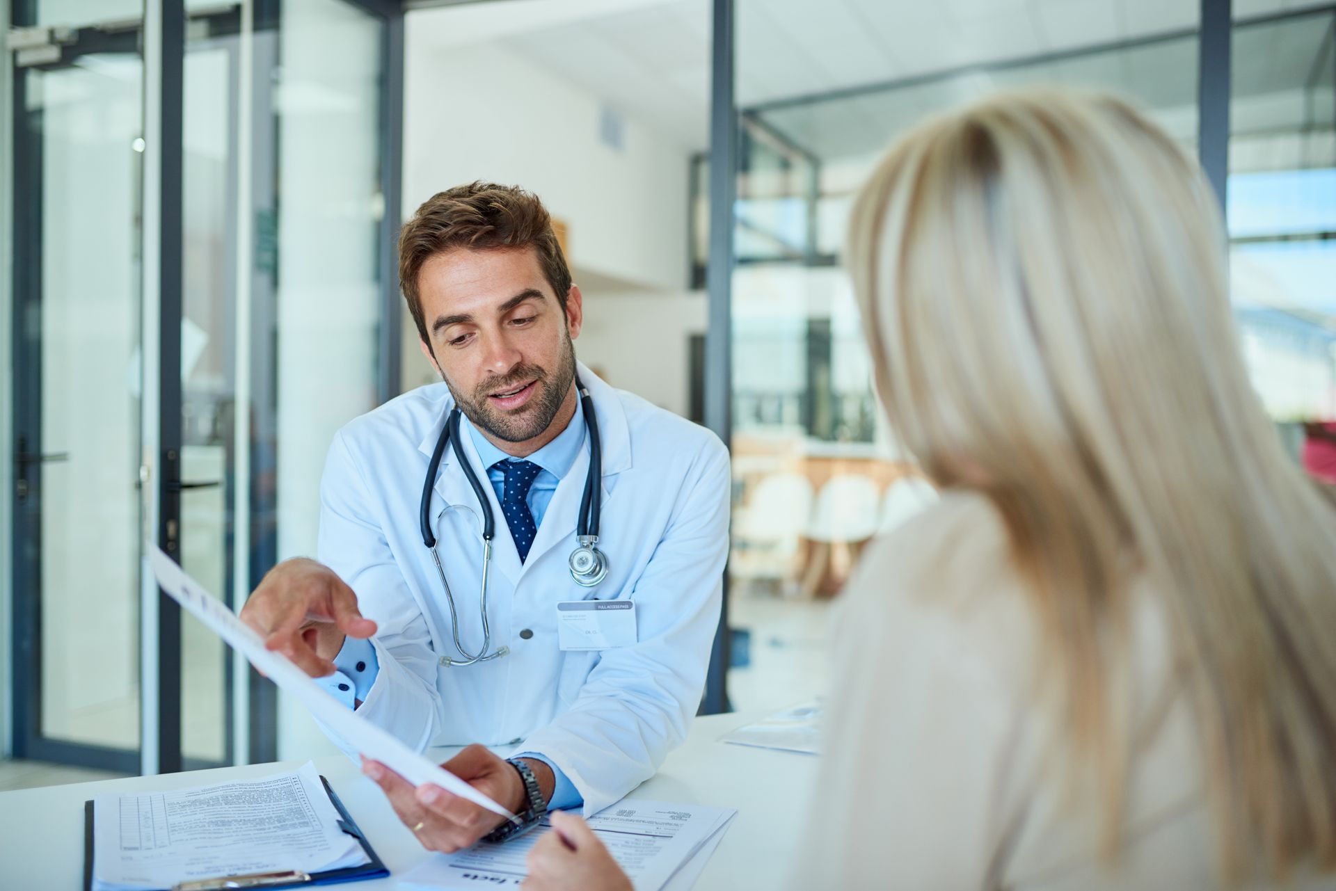 Doctor in lab coat pointing at paperwork, discussing results with a patient in an office.