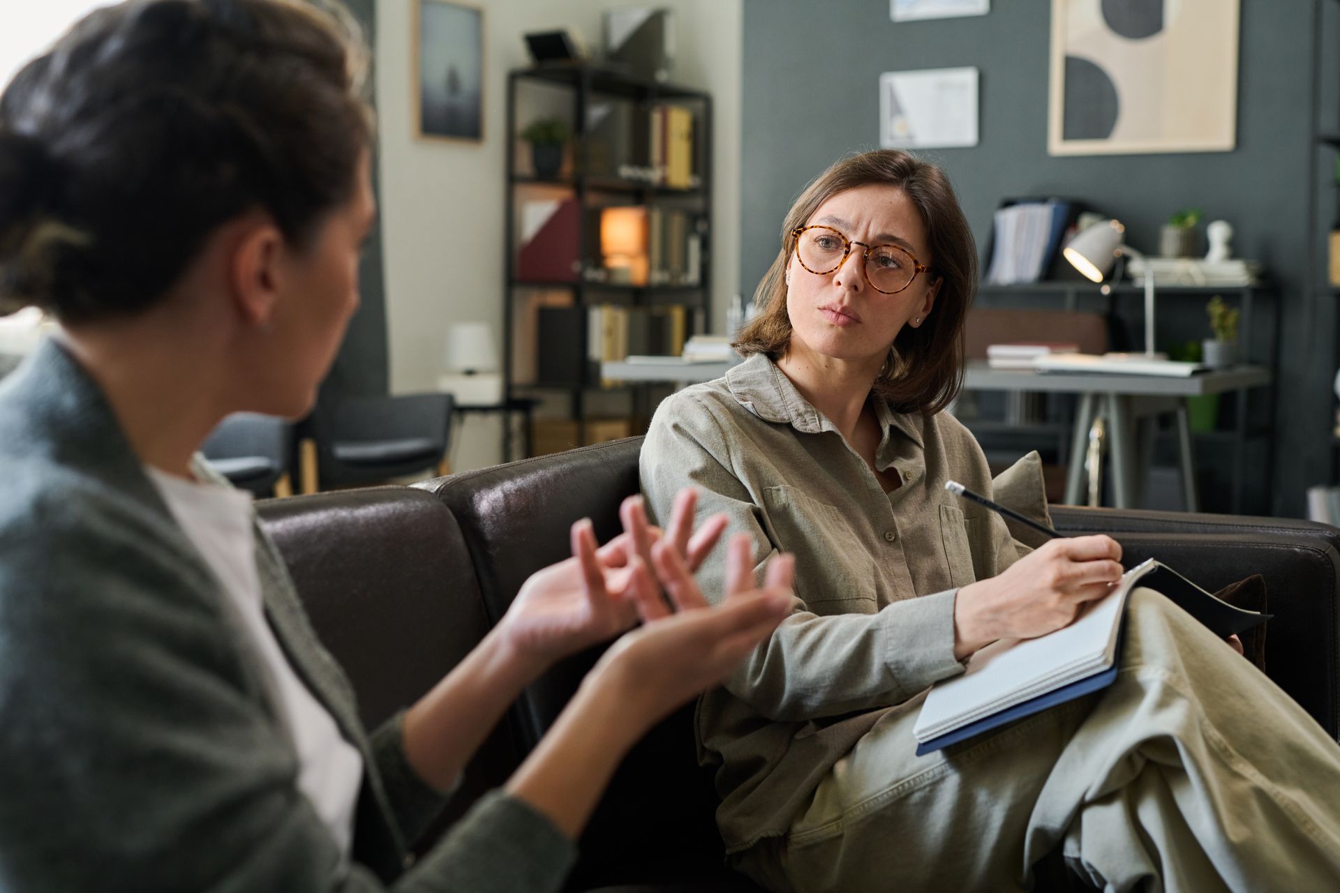 Woman gesturing while speaking to another woman taking notes on a couch in an office. Woman gesturing while speaking to another woman taking notes on a couch in an office.