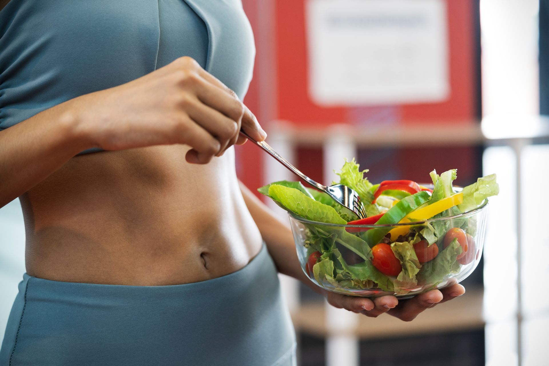 Woman in workout clothes holding a bowl of salad, ready to eat.