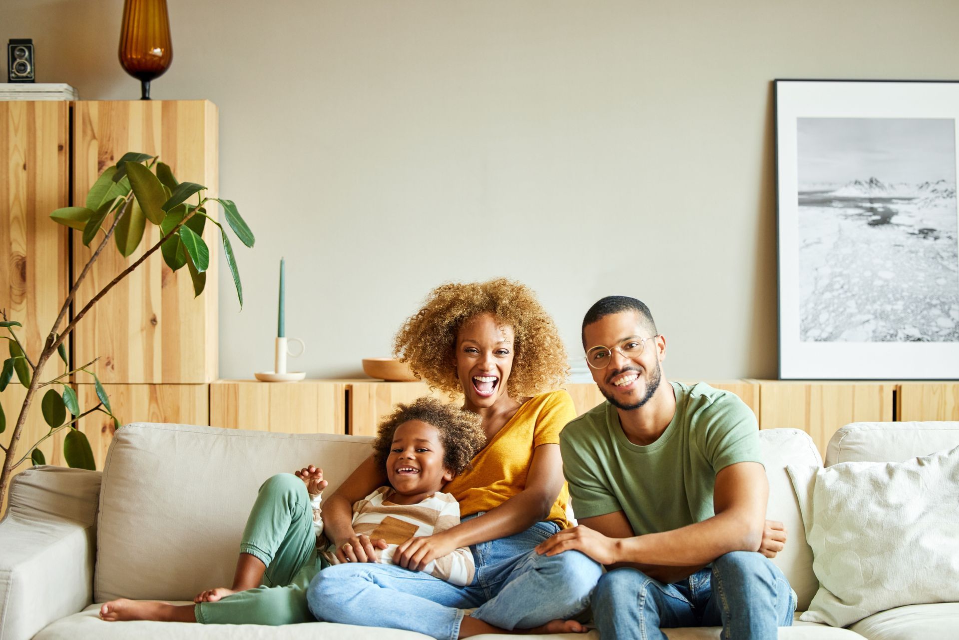 Family of three smiles on a sofa in a living room.