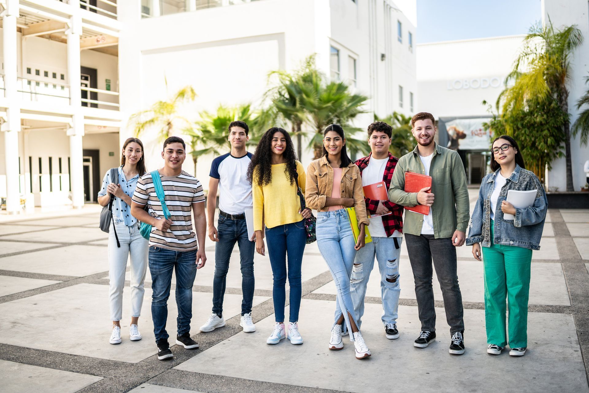 Group of students standing together on a campus, smiling. Buildings in the background.