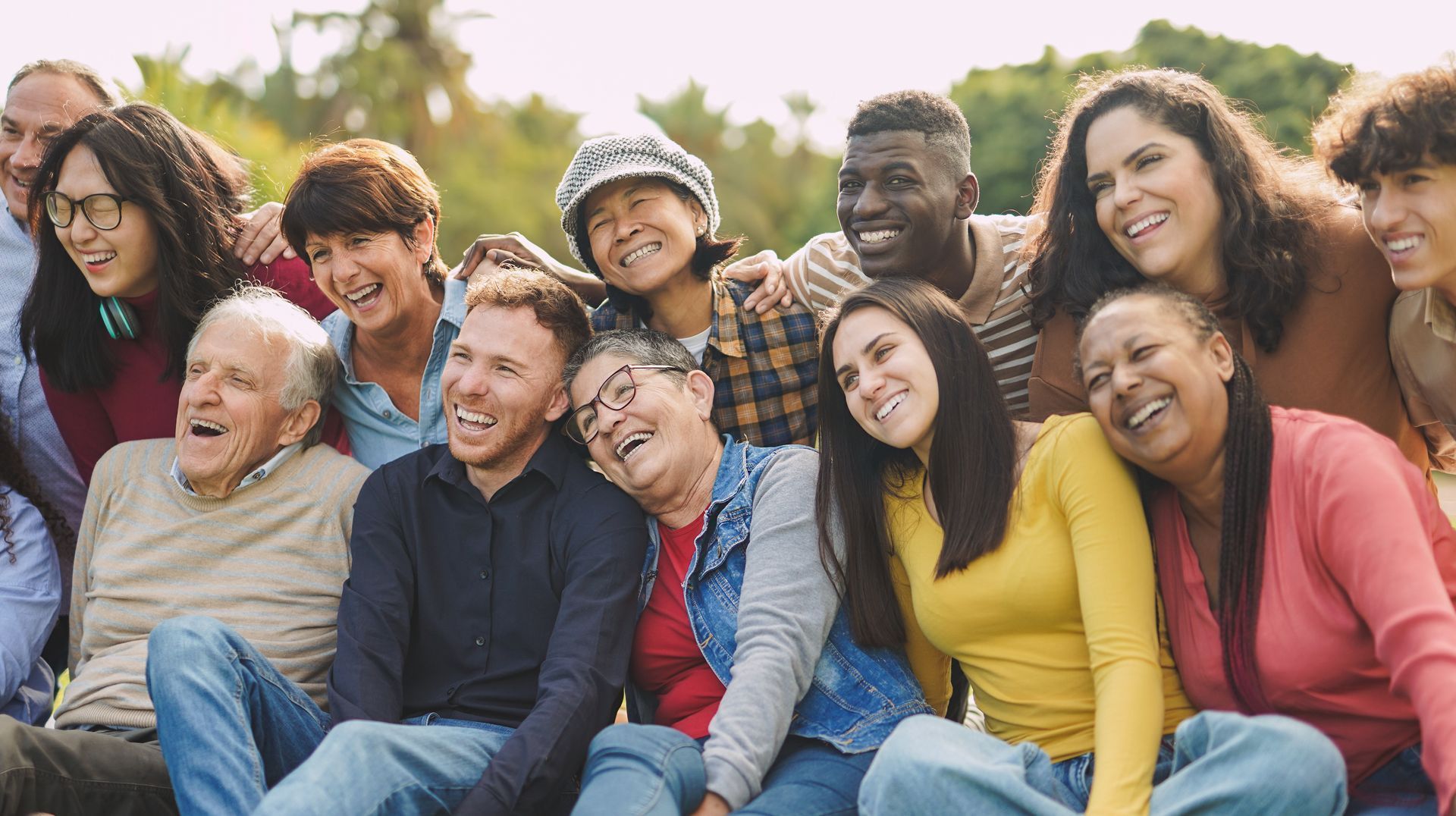 Group of diverse people smiling and laughing outdoors in the sunlight.