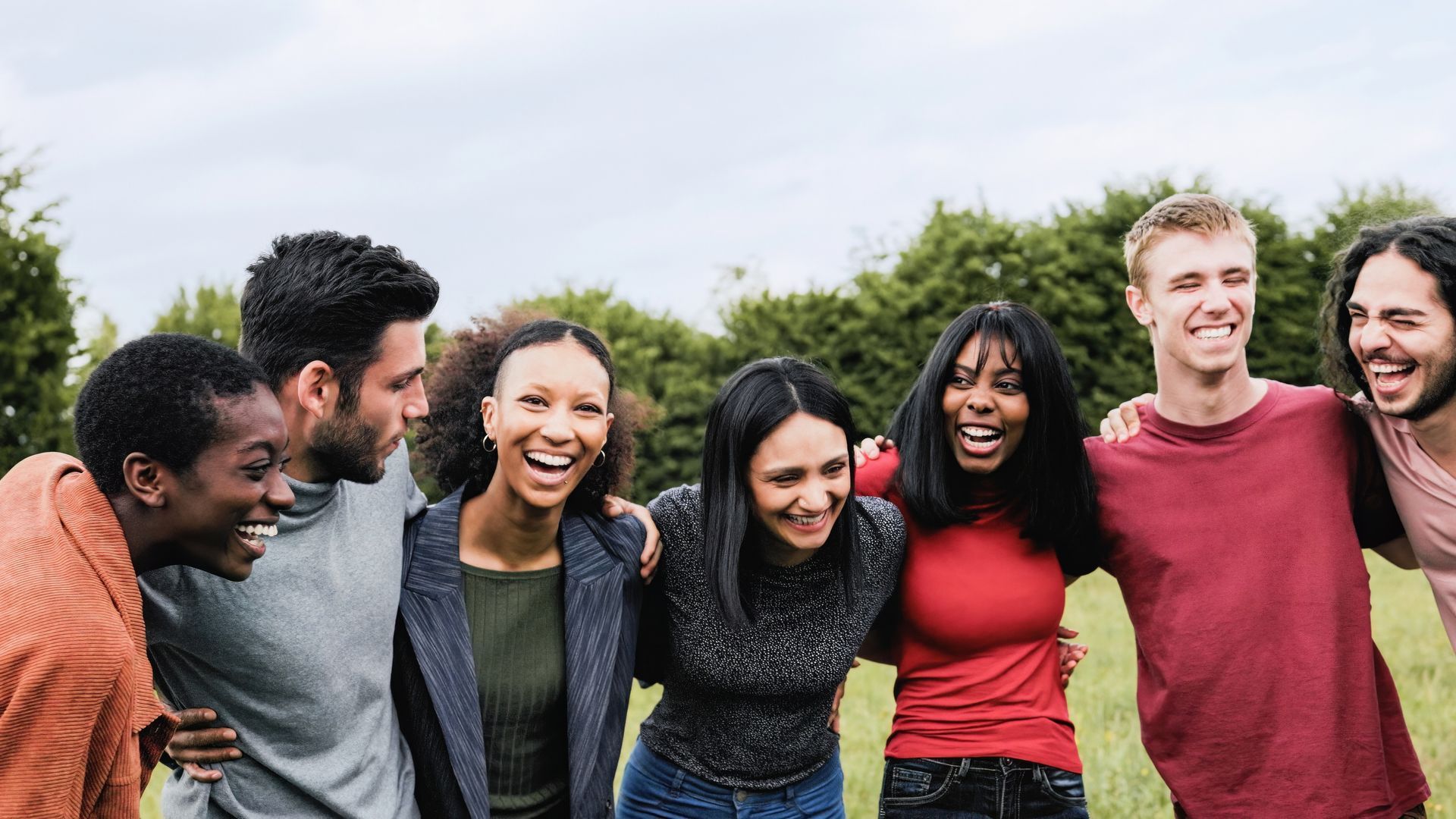A group of people with arms around each other laughing in a field.