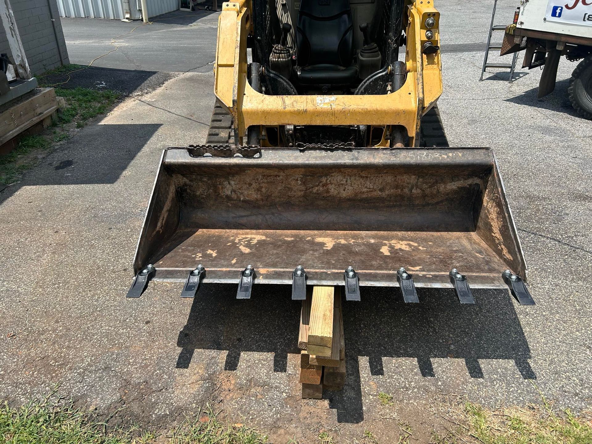 Yellow skid steer loader with bucket and teeth, parked on asphalt.