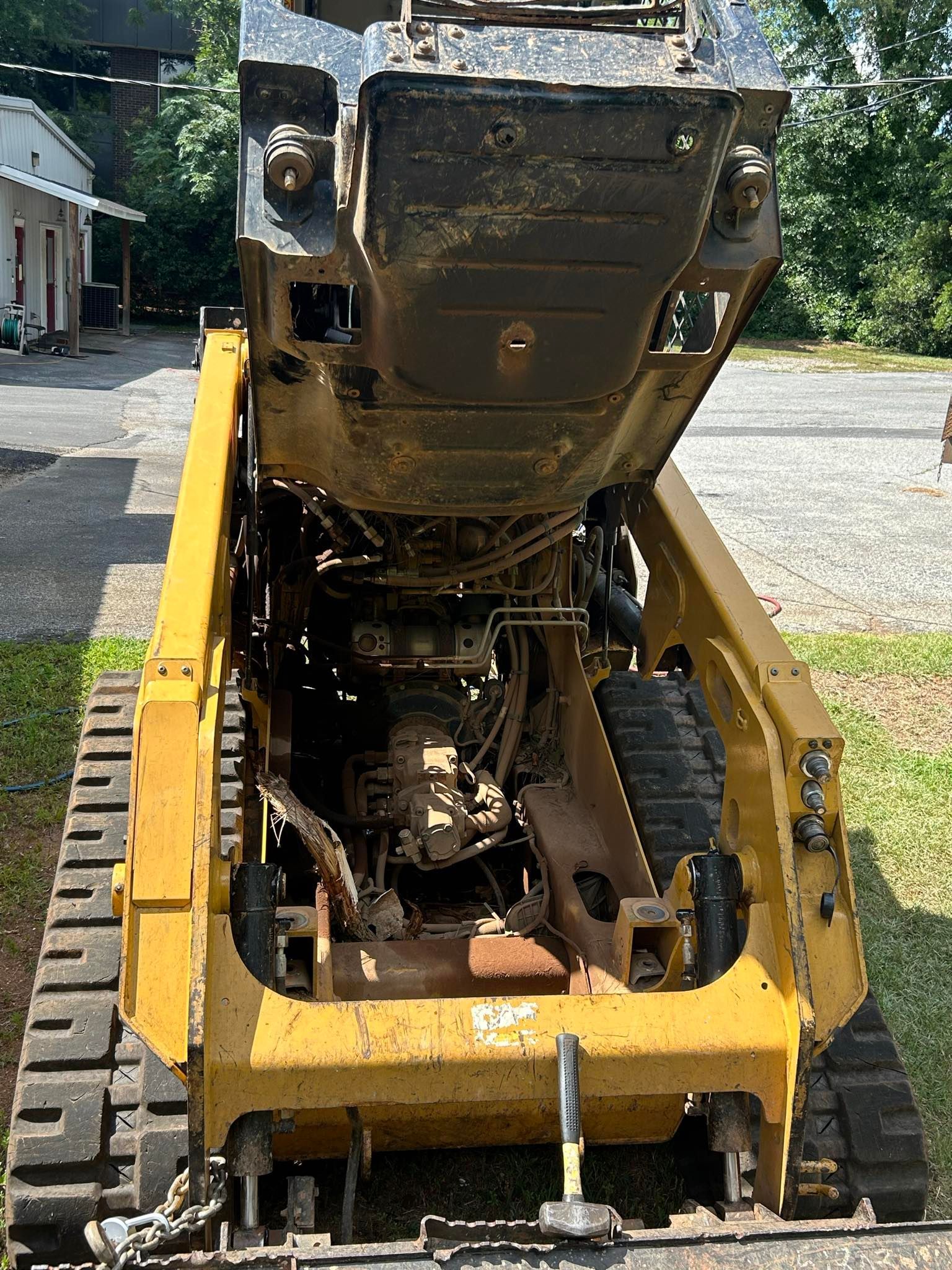 Yellow skid steer with engine exposed, parked outdoors.