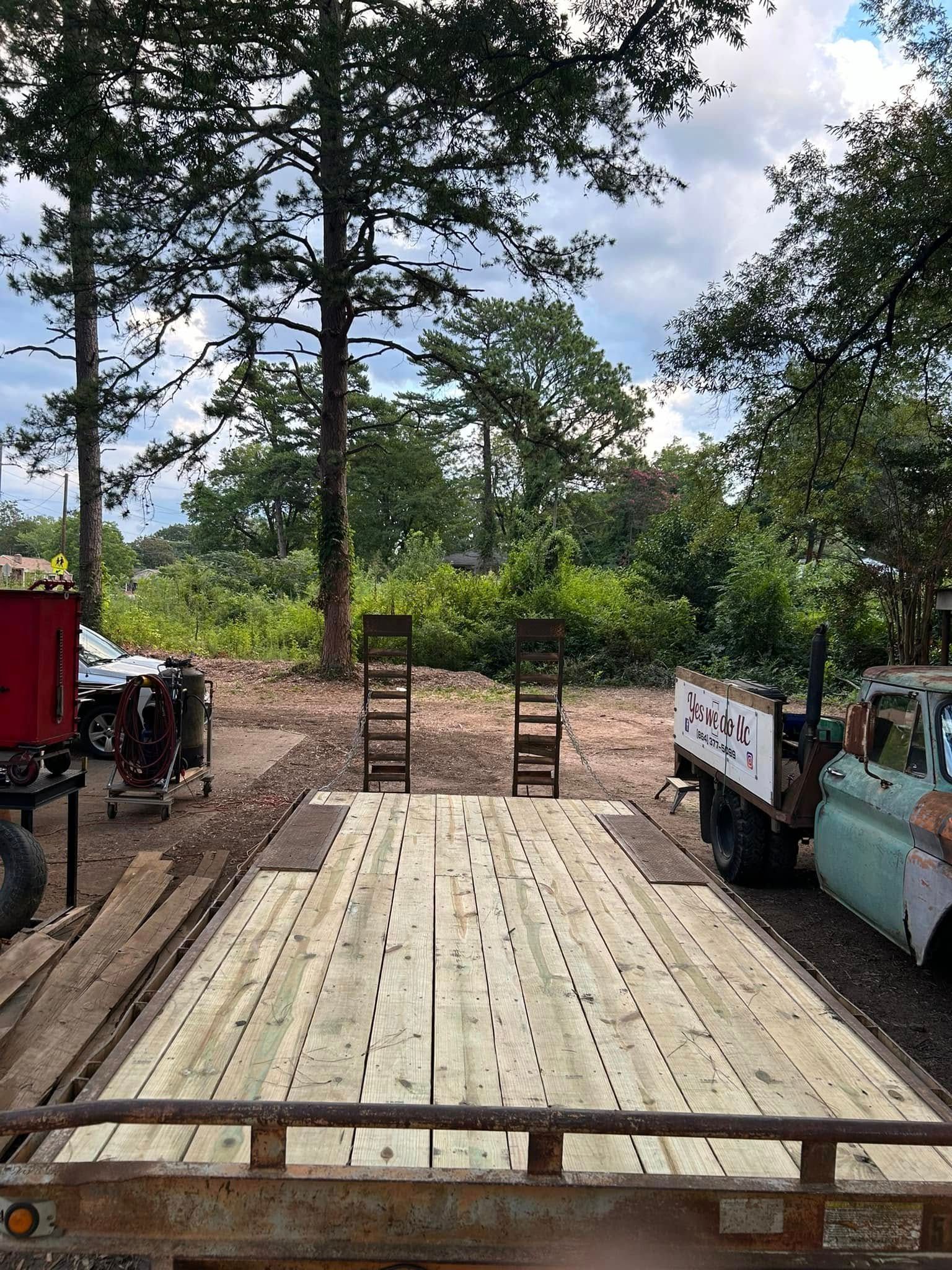 Wooden deck of a trailer with two chairs, trees, and a truck in an outdoor setting.