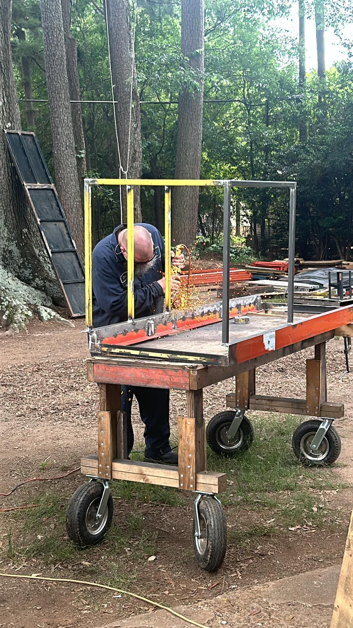 Man welding metal on a cart outdoors.