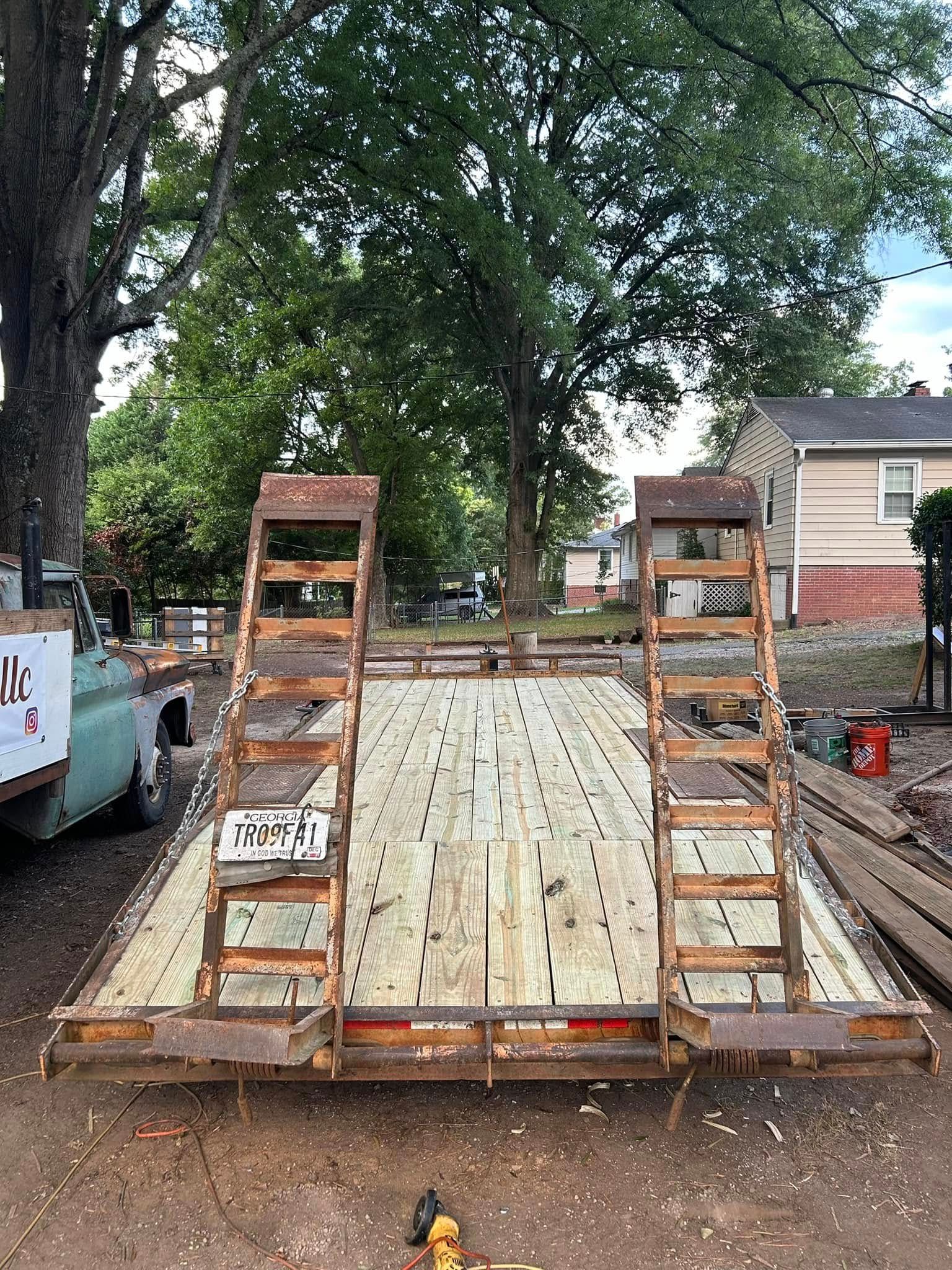 Trailer with wooden deck and ramps, parked outdoors in front of a house.