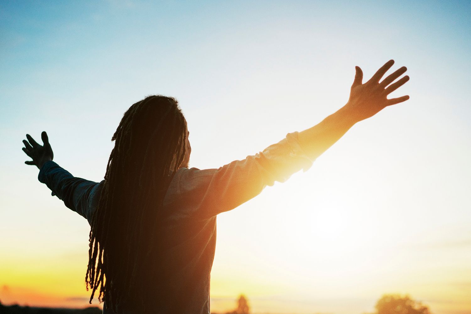 A woman is standing with her arms outstretched at sunset.
