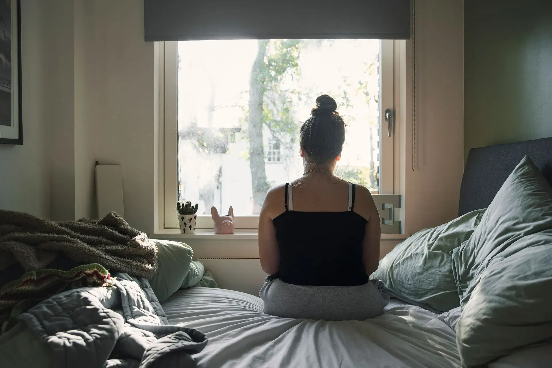 A woman is sitting on a bed looking out of a window.