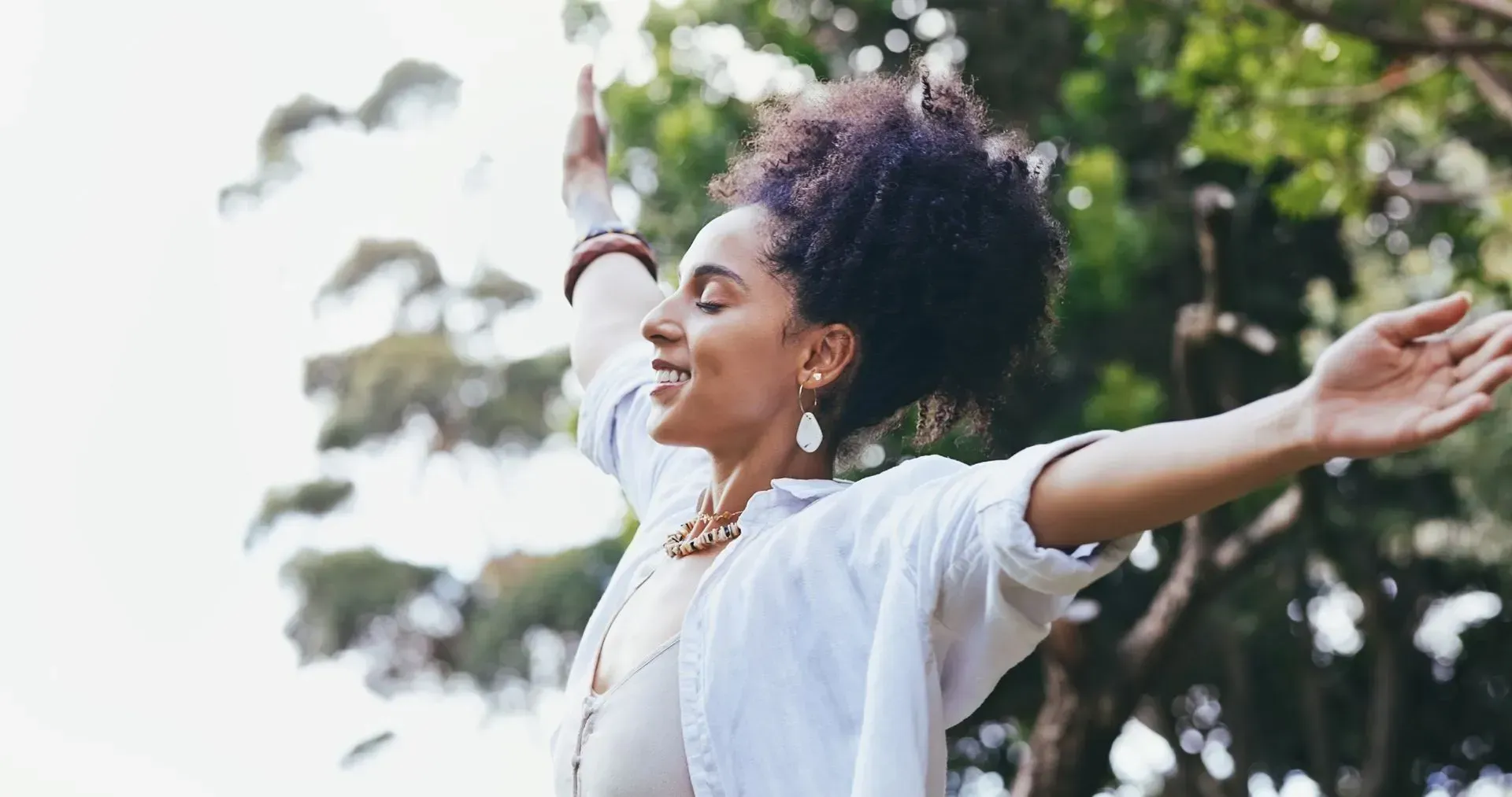 A woman is standing in front of a tree with her arms outstretched.