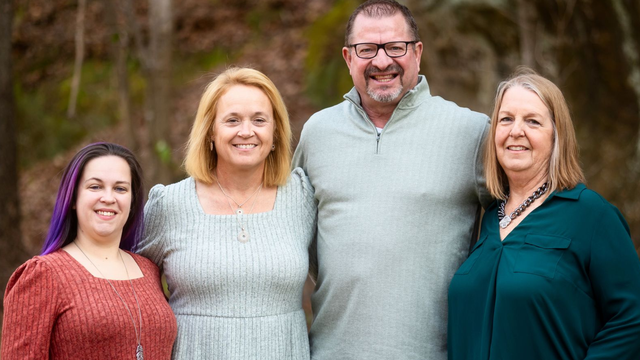 Four people pose together outdoors; two women, a man, another woman smile.