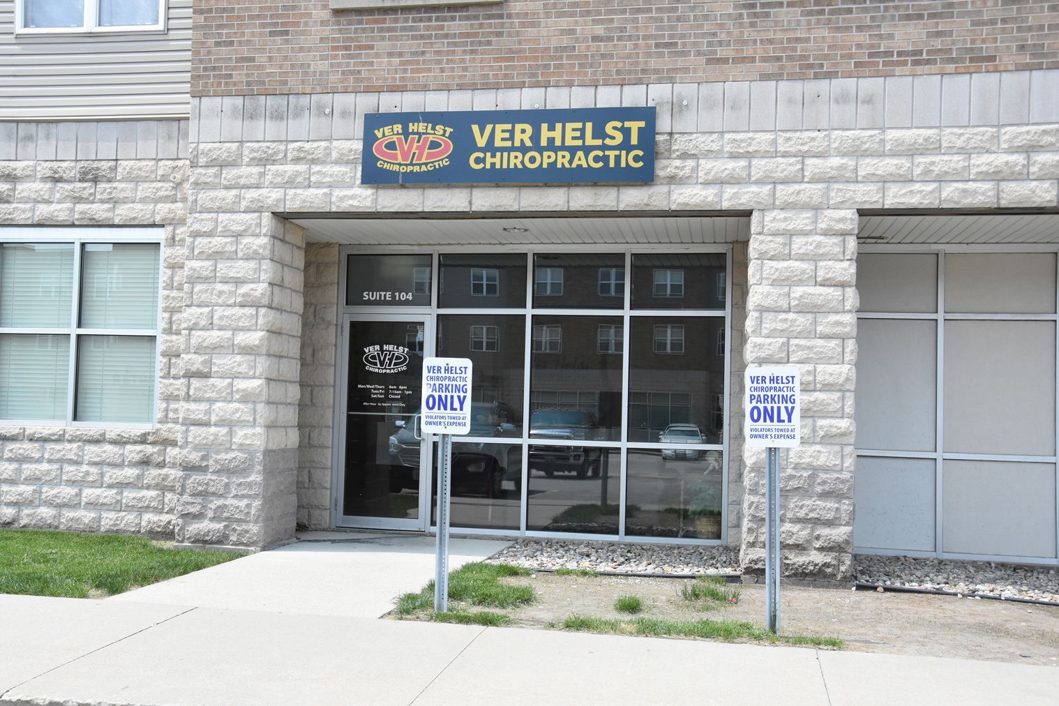 Entrance to Ver Helst Chiropractic clinic with stone facade, glass door, parking signs.
