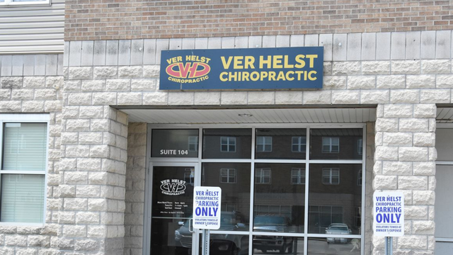 Entrance to Ver Helst Chiropractic clinic with stone facade, glass door, parking signs.