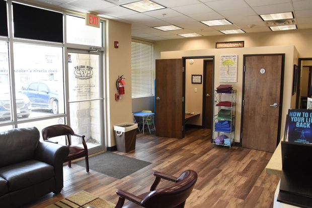 Interior of a waiting area with a glass door, chairs, and multiple closed doors. Wooden floors.